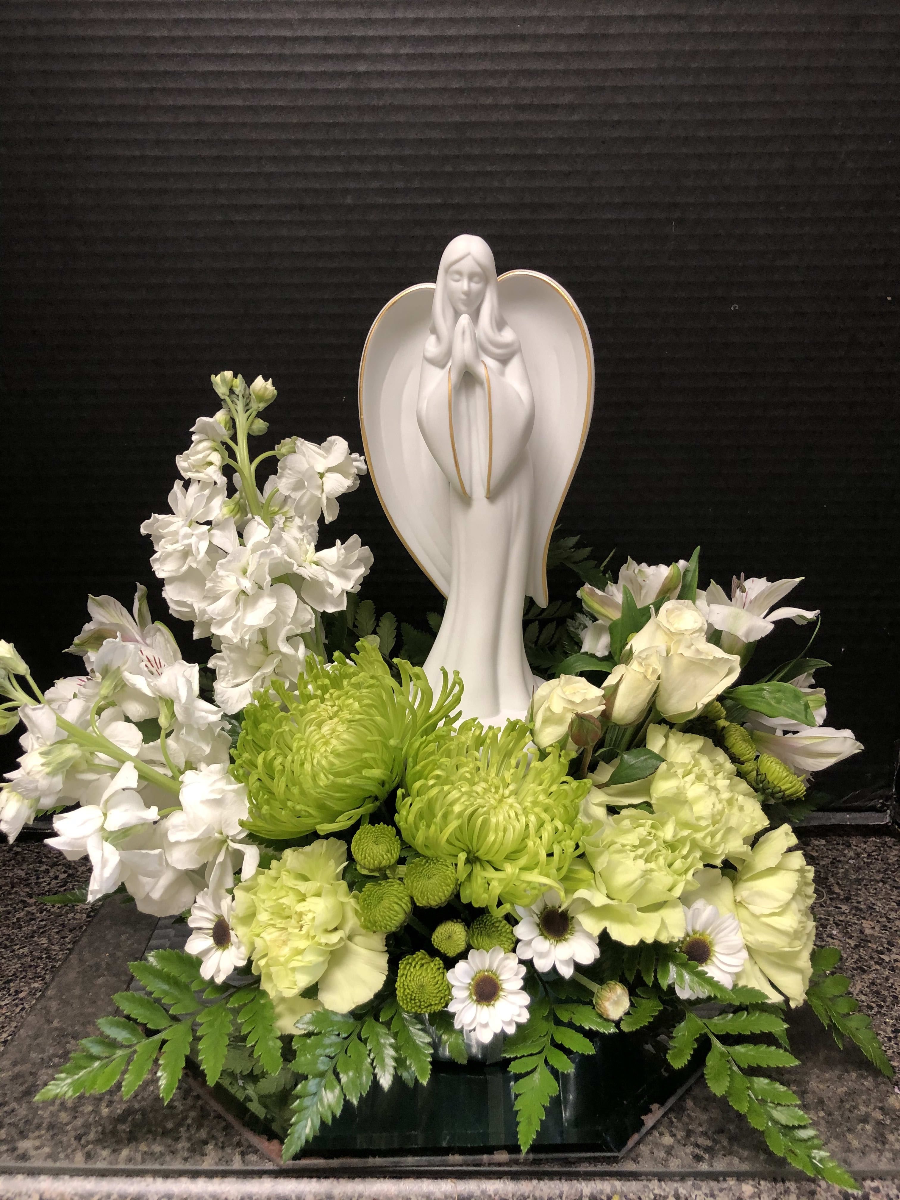 White floral arrangement with a praying angel statue in the center