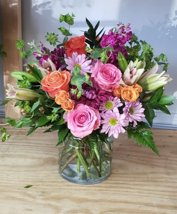 Mixed bouquet of pink, peach, and purple flowers in a glass vase