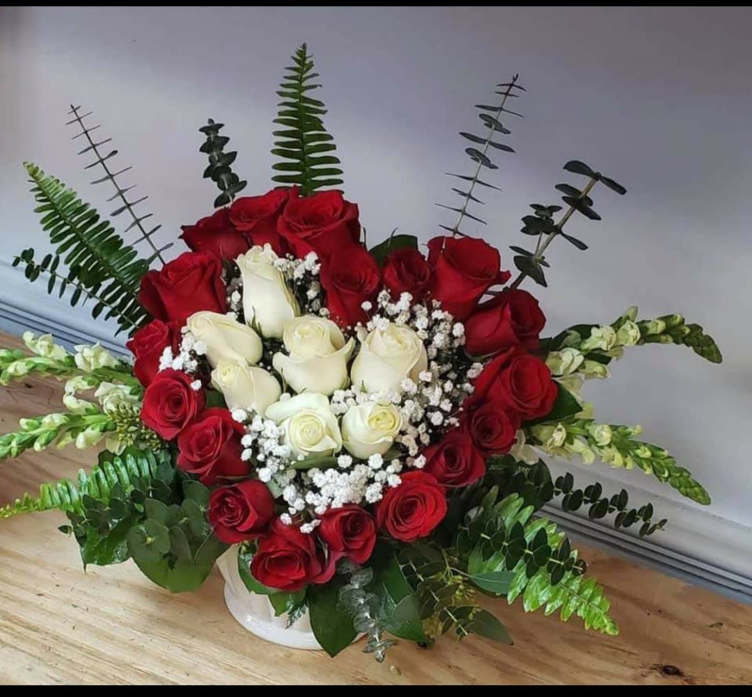 Red and white roses arranged in a white vase with baby's breath