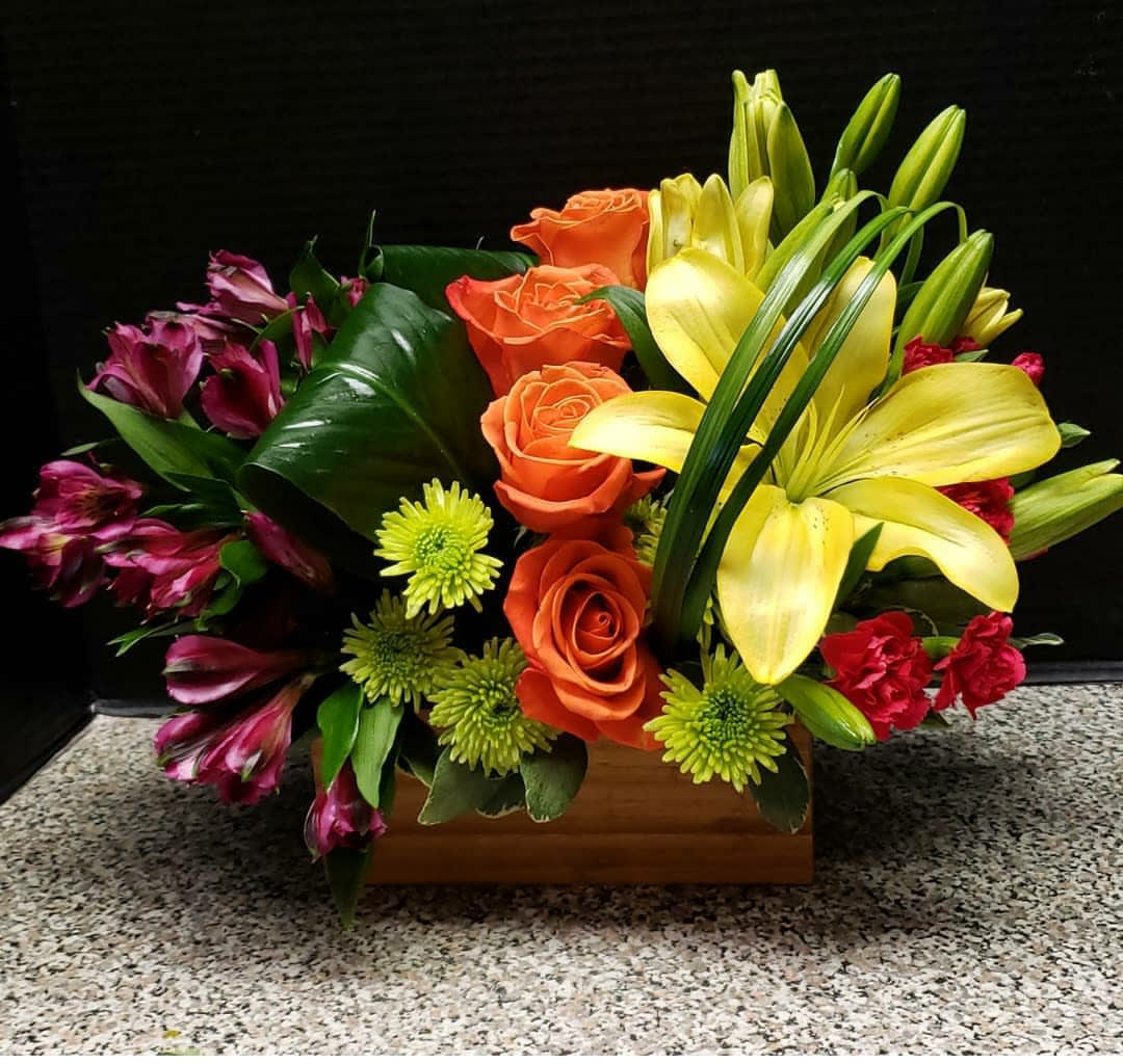 Mixed bouquet with yellow lilies, orange roses, and purple alstroemeria in a wooden box