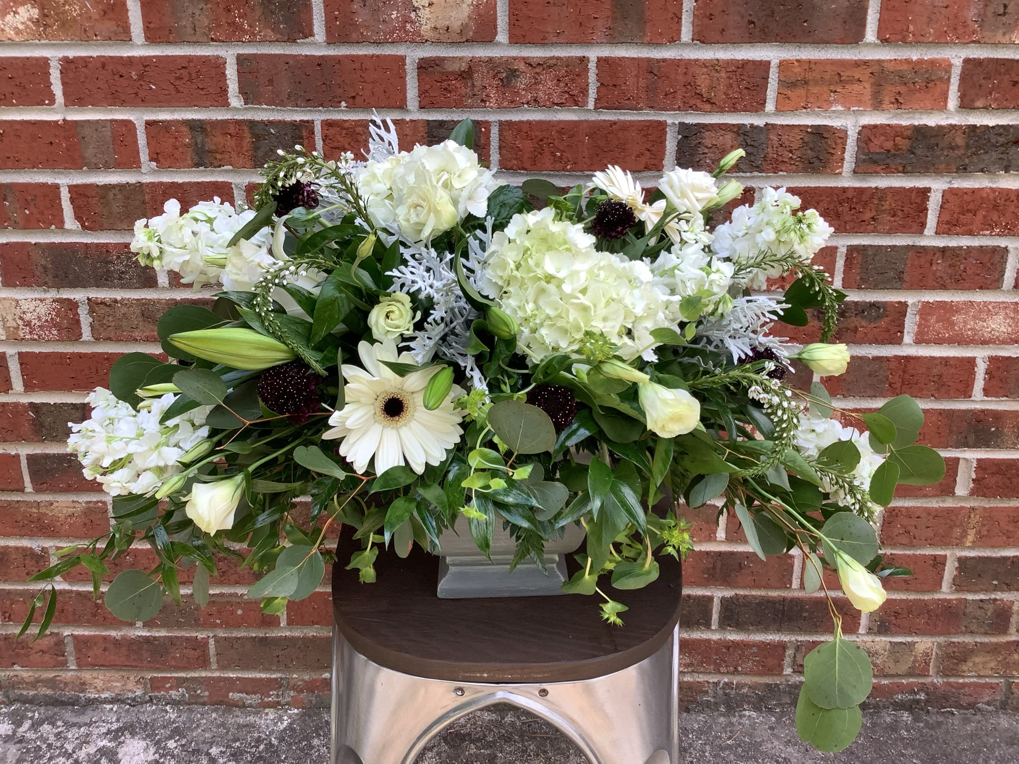 White floral arrangement in a gray vase with mixed greenery