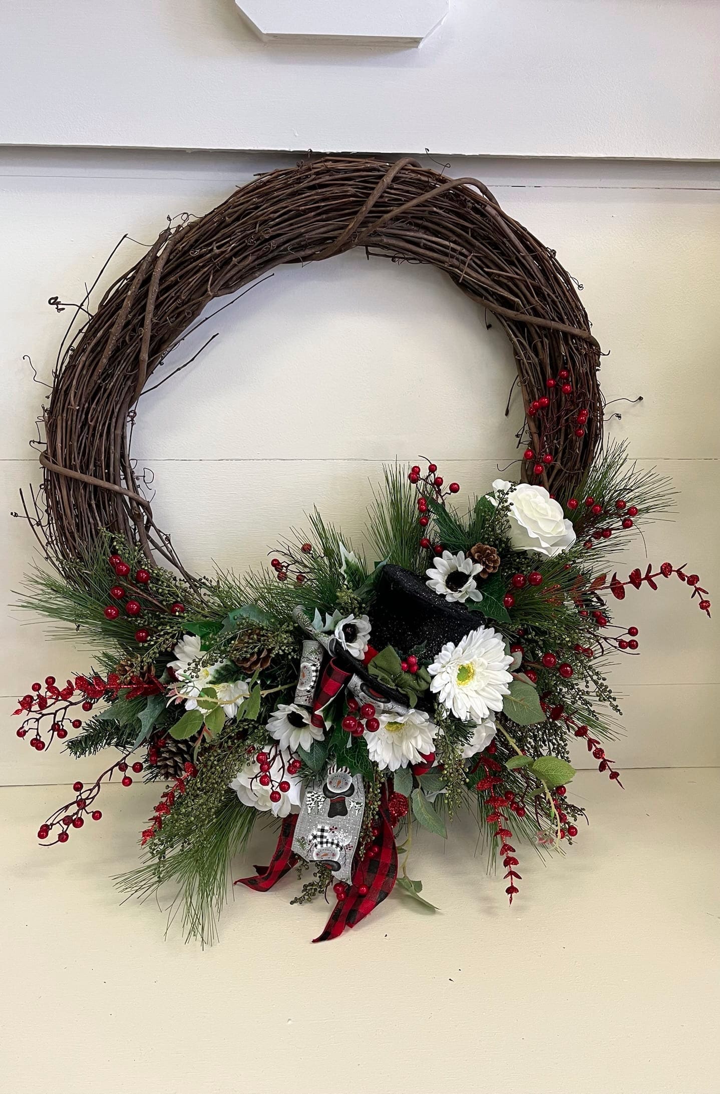 Holiday wreath with white flowers, red berries, and a plaid ribbon