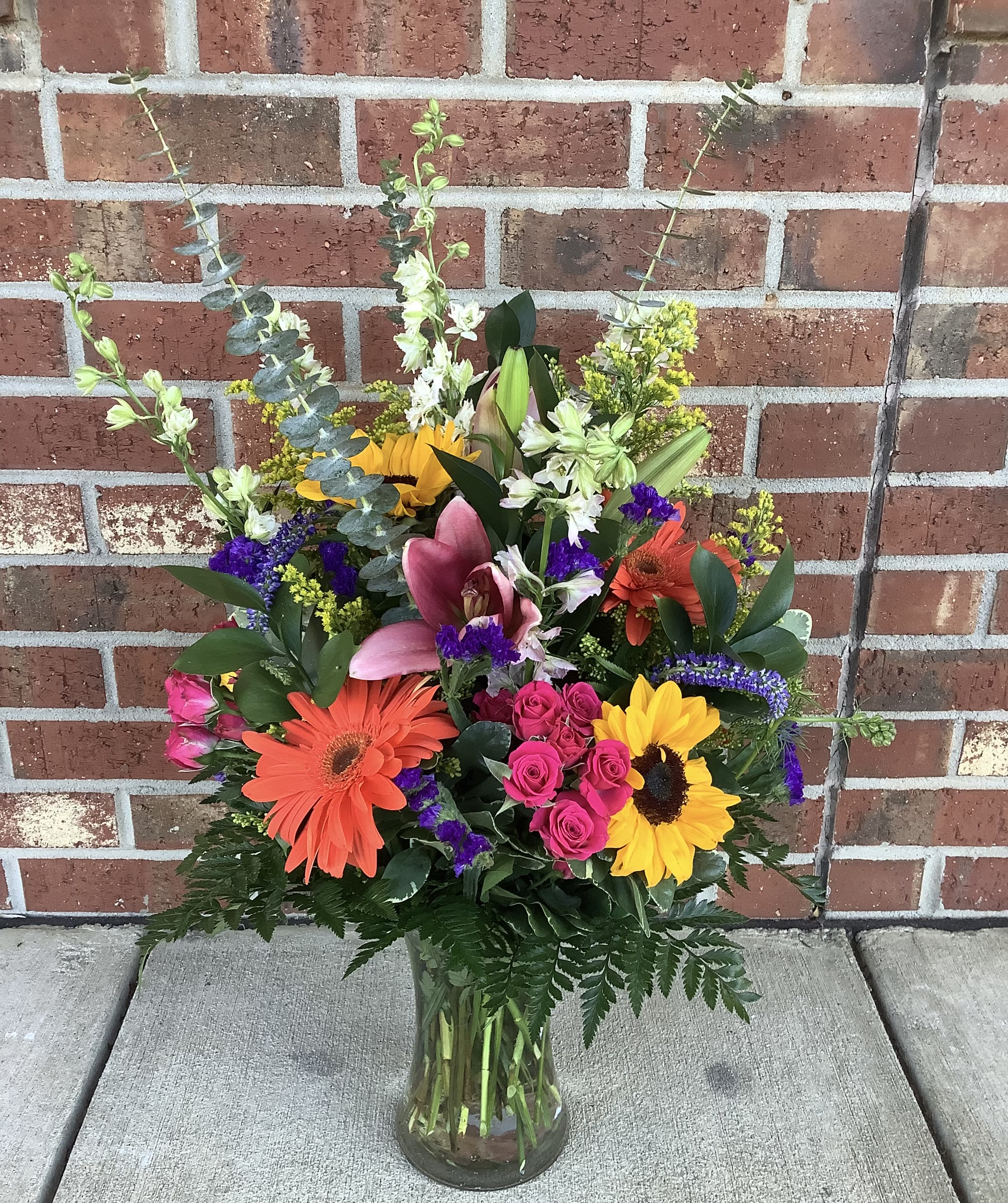 Colorful mixed bouquet in a clear glass vase with lilies, gerberas, roses, and sunflowers