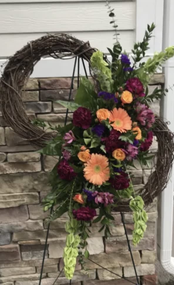 Floral standing spray with orange and purple flowers on a wreath stand