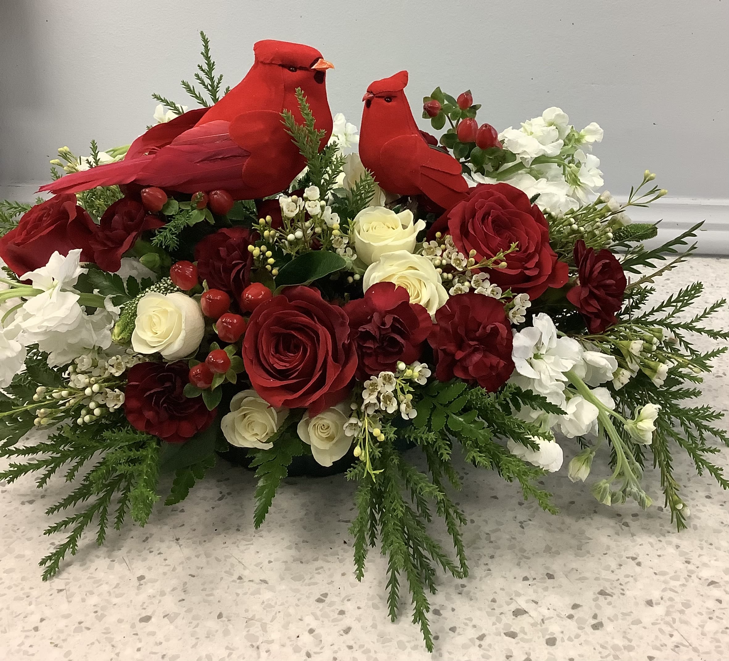 Red cardinal figurines sit in a red and white floral arrangement with roses.