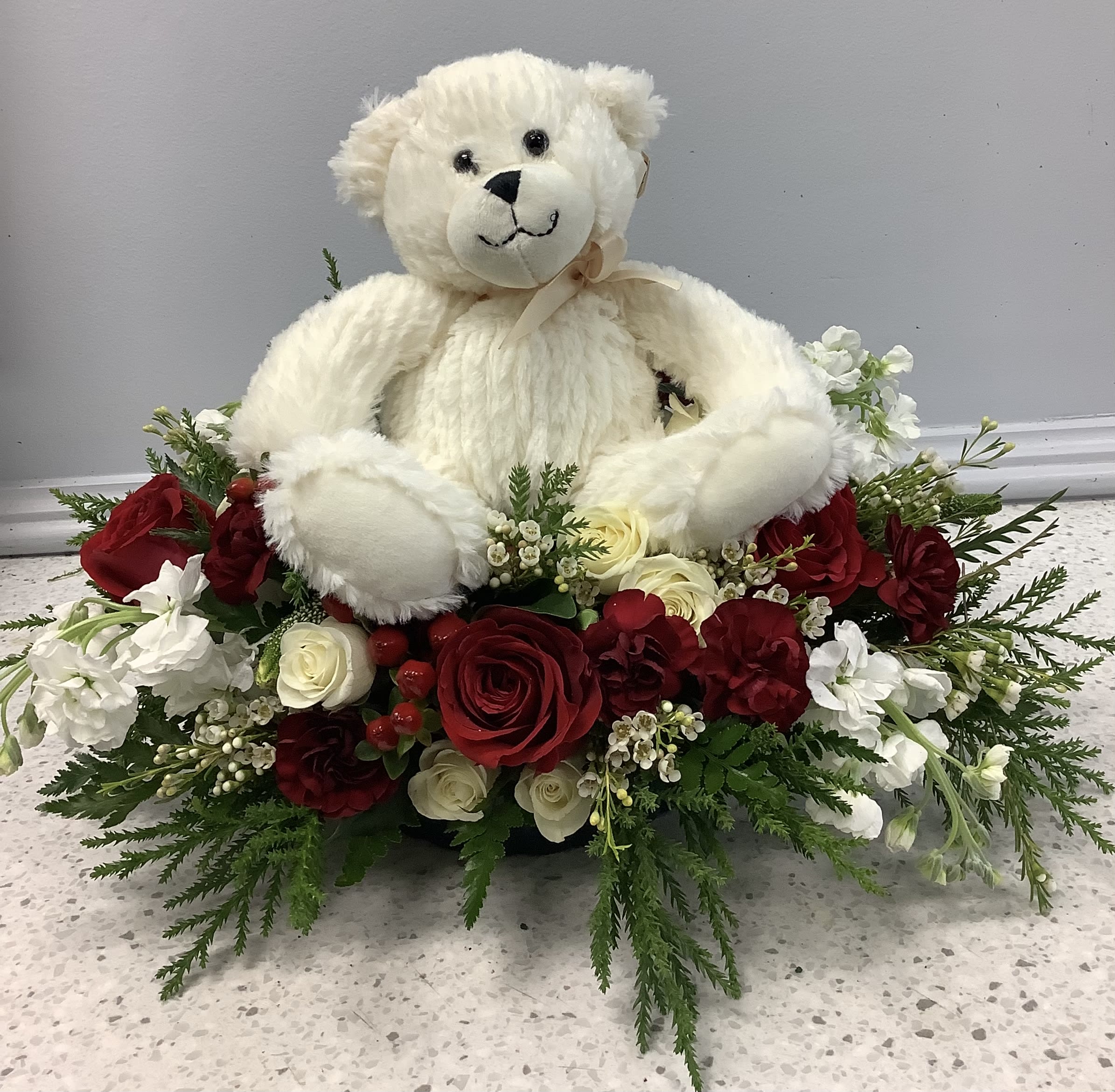 White teddy bear sitting in a red and white rose arrangement