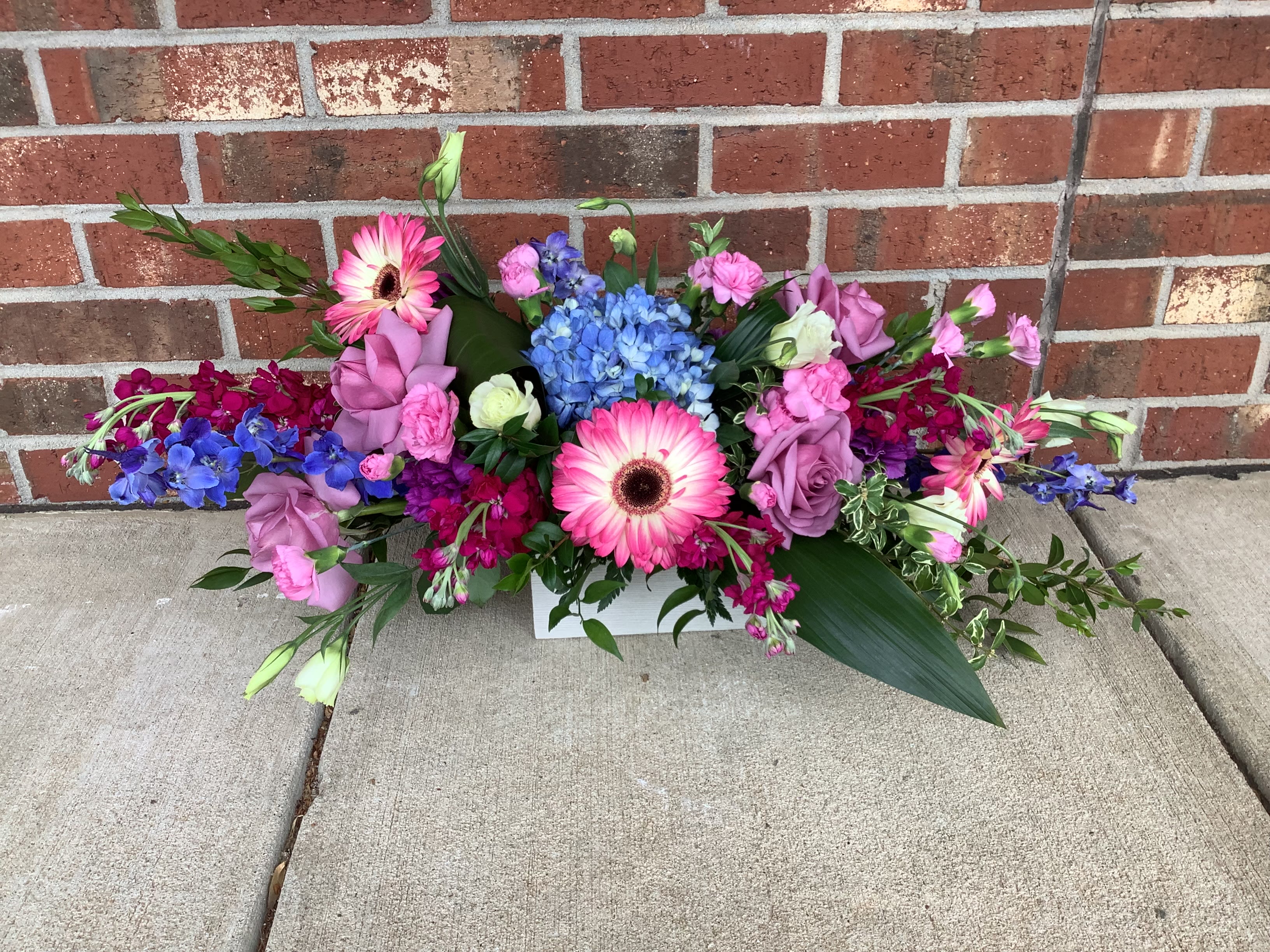 Colorful mixed flower arrangement with pink gerberas and roses in a white container