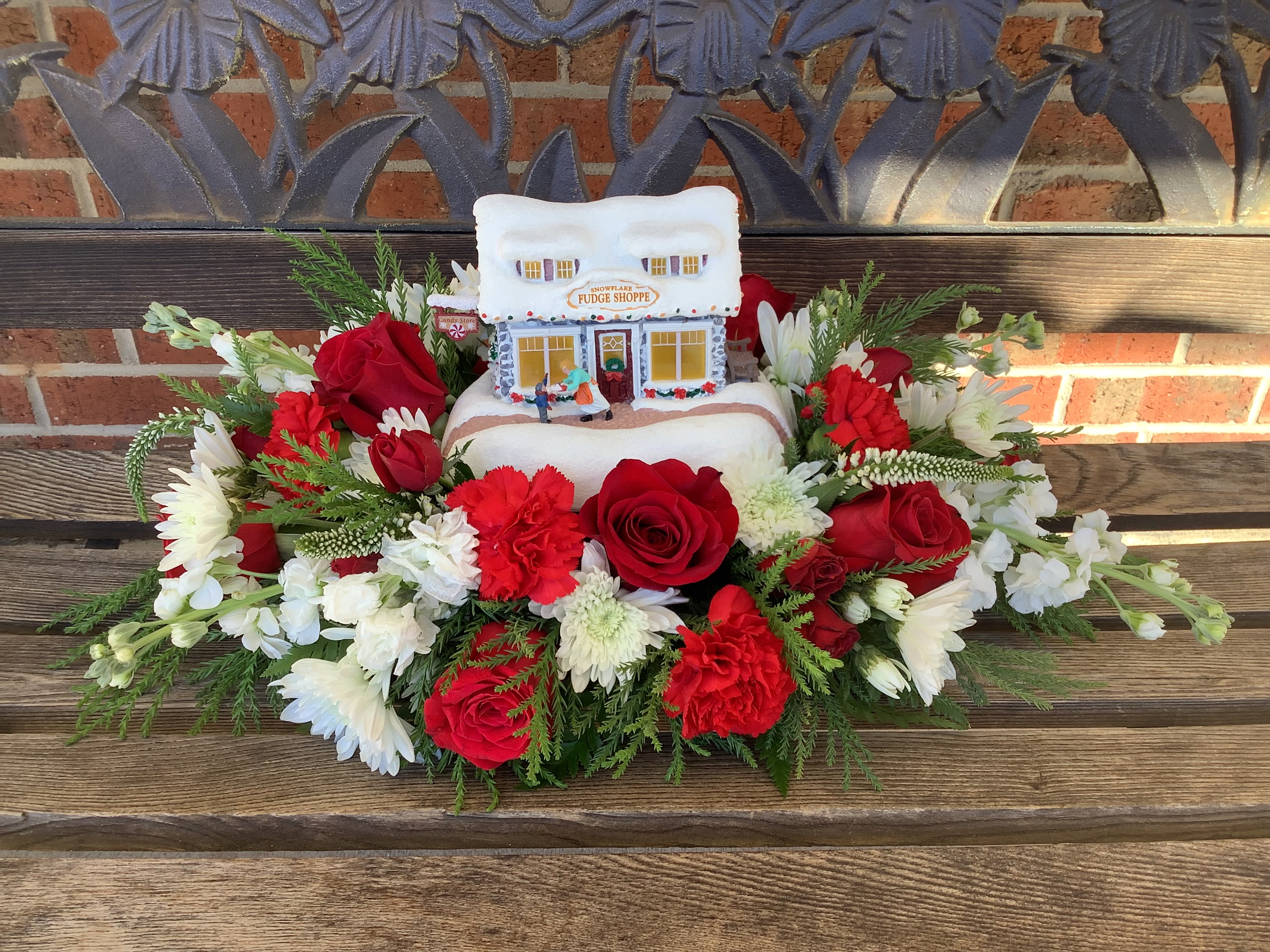 Red and white floral arrangement around a small snow-covered house decoration