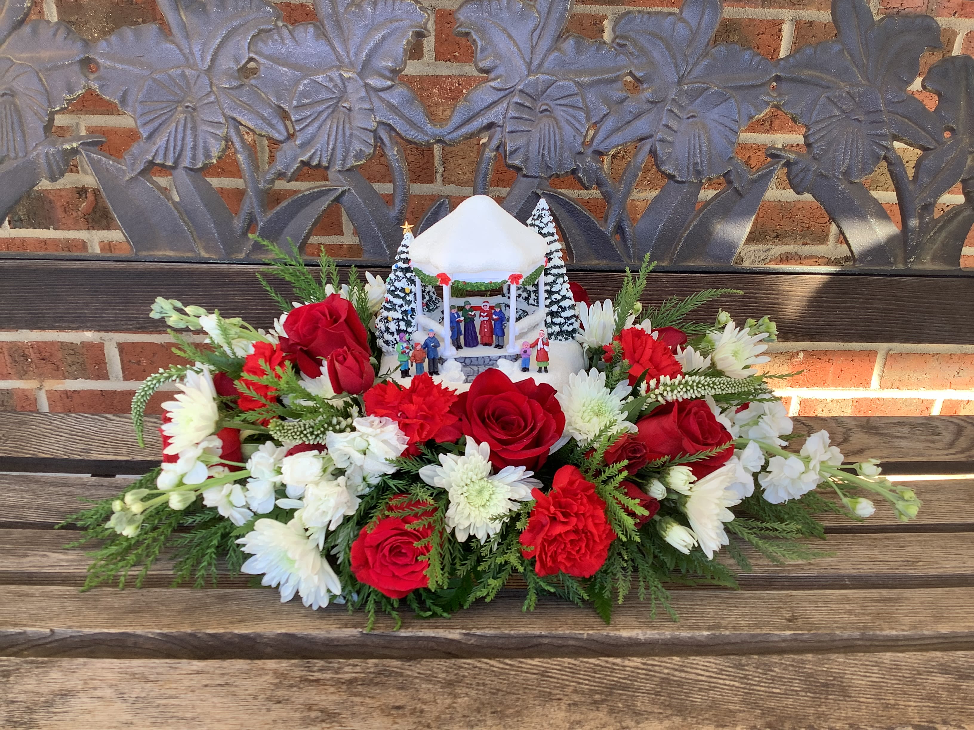Red roses and white flowers arranged around a small holiday gazebo centerpiece
