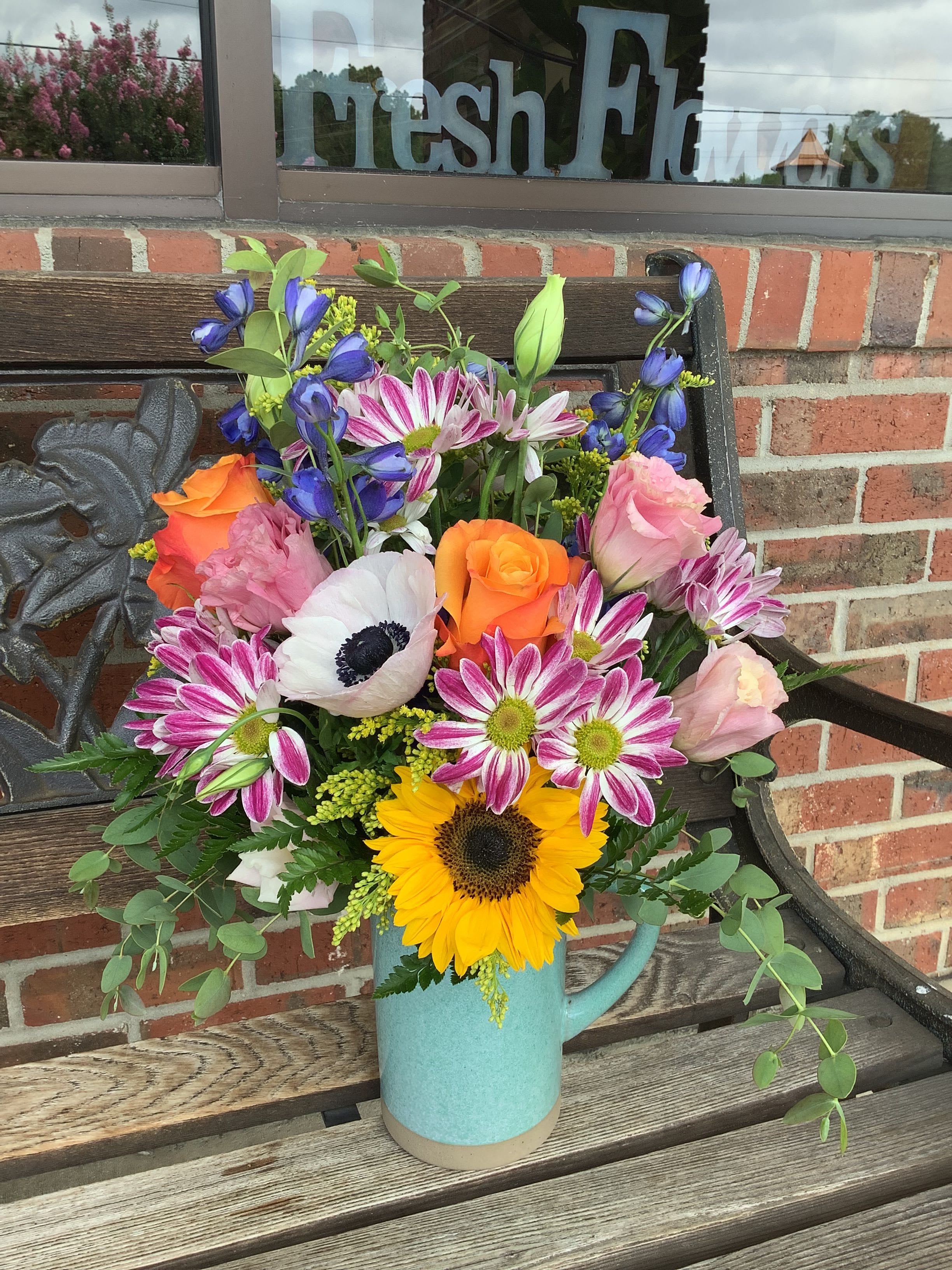 Mixed bouquet in a blue pitcher with sunflowers, roses, and daisies
