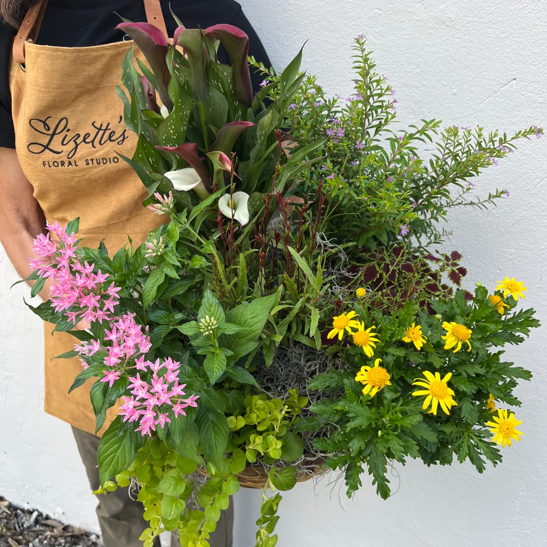 Person holding a large mixed floral basket with pink, yellow, and white blooms