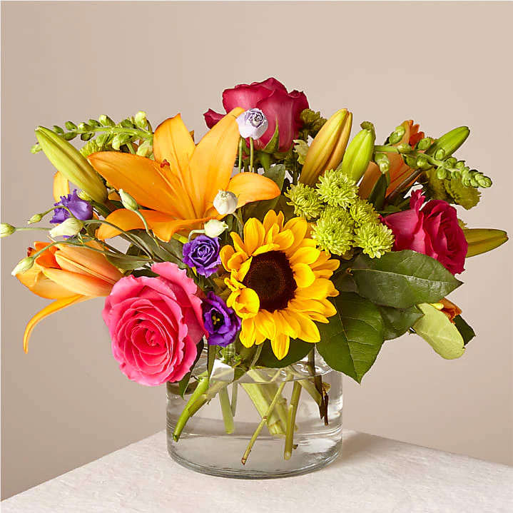 Bright mixed bouquet with sunflower, orange lilies, and pink roses in a clear glass vase