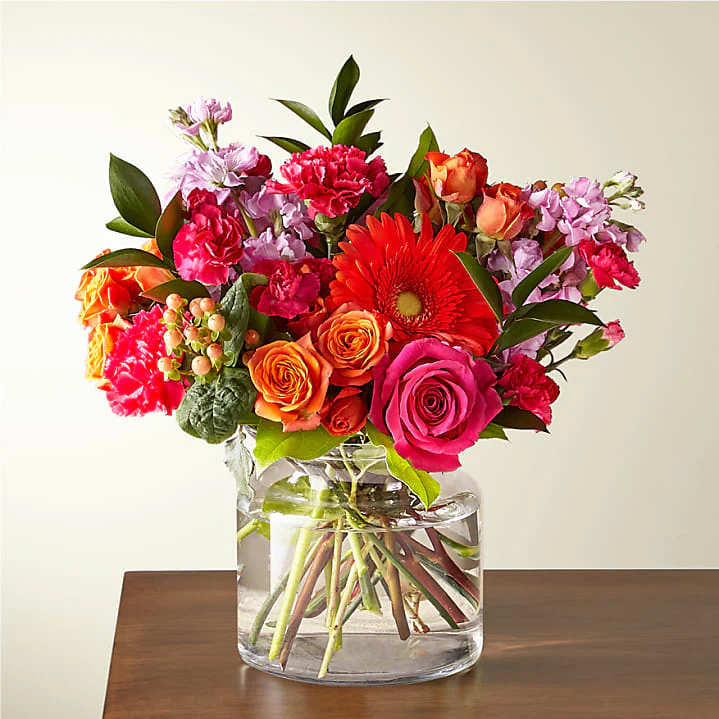 Bright bouquet of pink roses, orange roses, gerbera daisy and carnations in a round glass vase