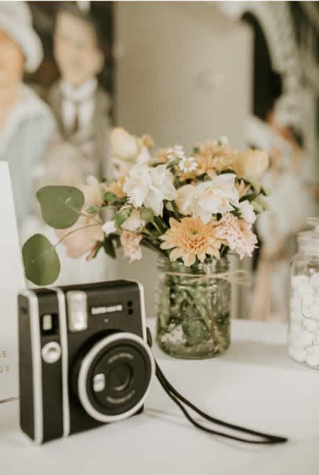 Small pastel flower arrangement in a glass jar beside a camera