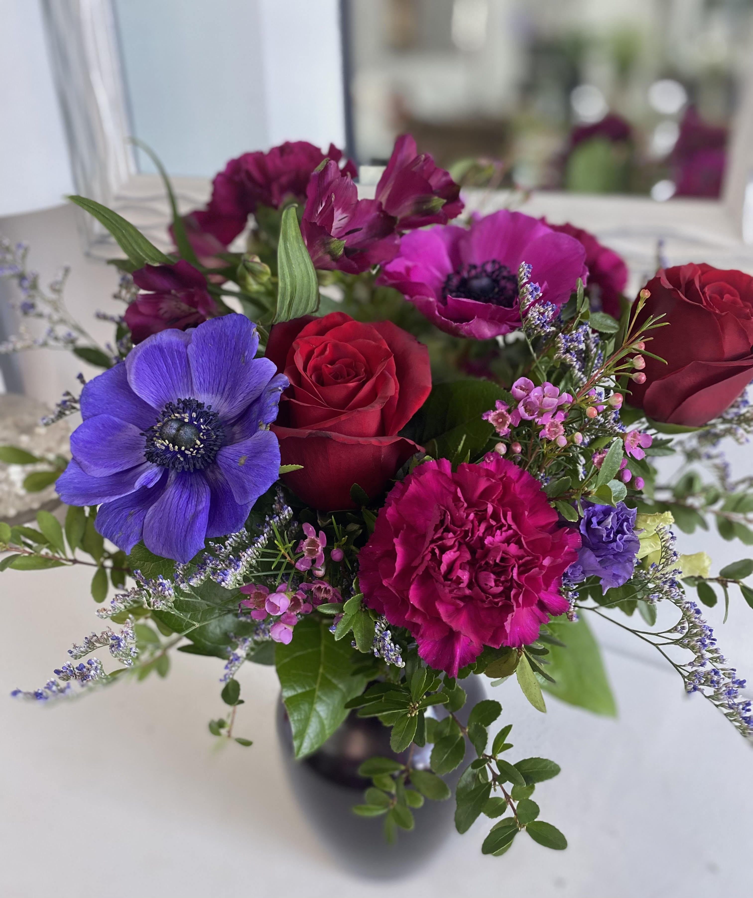 Vase arrangement of red roses, magenta carnations, and purple anemones with small pink blooms