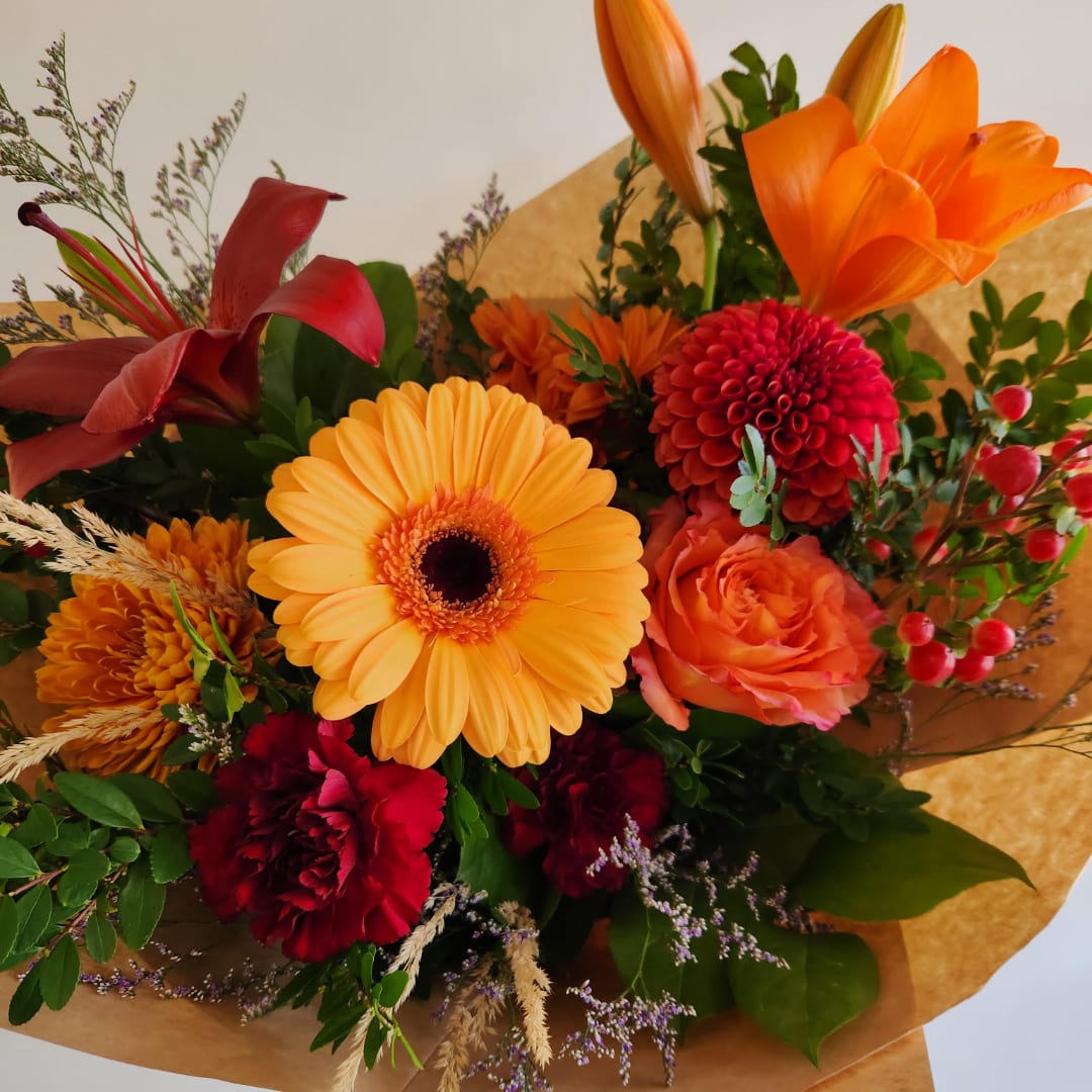 Mixed bouquet with orange, red, and yellow flowers wrapped in brown paper