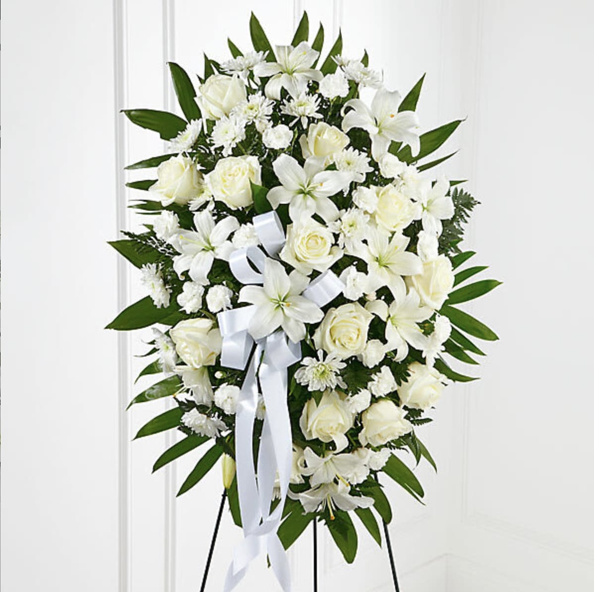 White floral standing spray with roses and lilies on a white ribboned easel