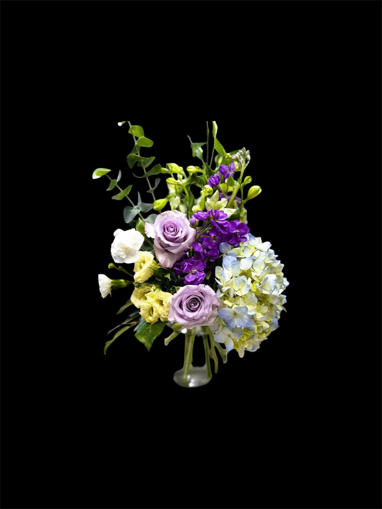 Lavender roses, hydrangea, and purple flowers in a clear vase