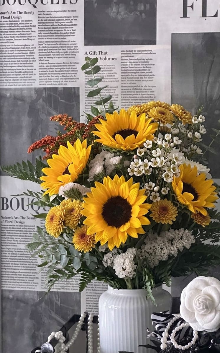 Bouquet of sunflowers, white filler flowers, and yellow mums in a white vase