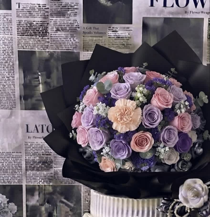 Bouquet of pink and lavender roses with a peach carnation in black wrap