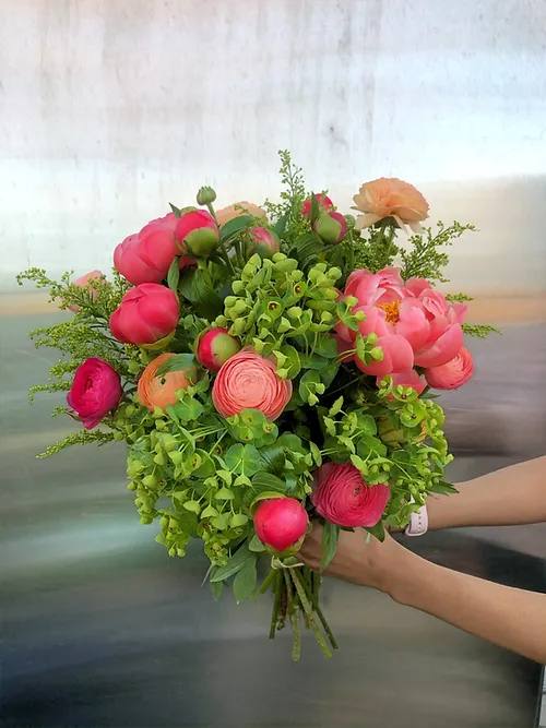 Handheld bouquet of pink and peach flowers with lush greenery