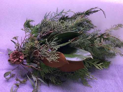 A loose evergreen floral arrangement with a pinecone on a purple background.