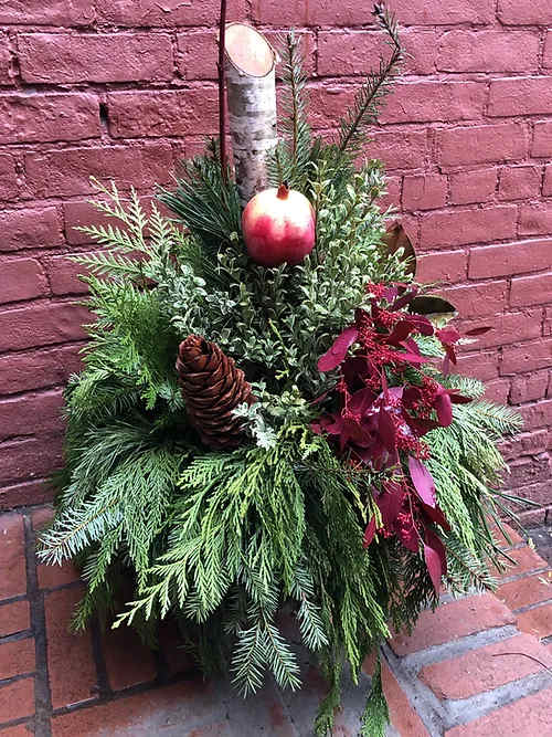 Holiday greenery arrangement with a pinecone and red ornament on a birch log