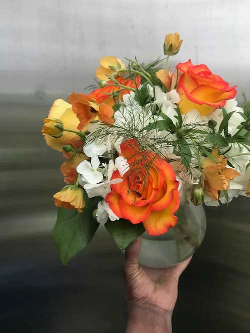 Bouquet of orange and yellow roses with white flowers in a glass vase