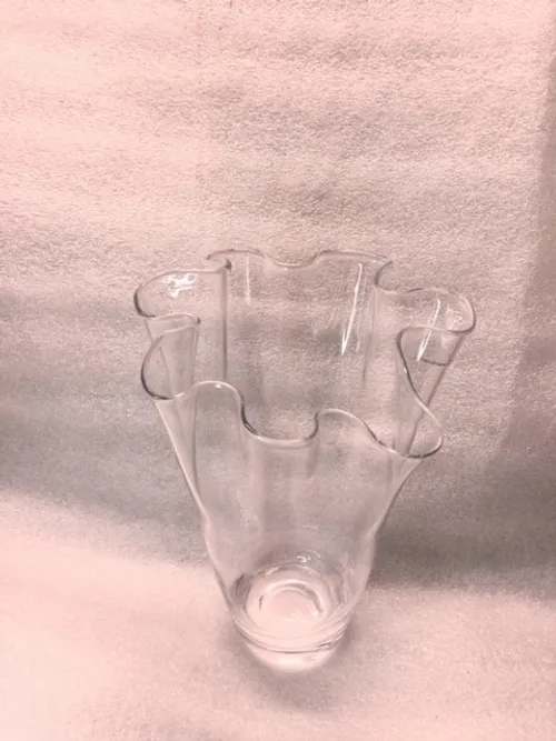 Clear glass vase with a wavy flared rim on a soft pink background
