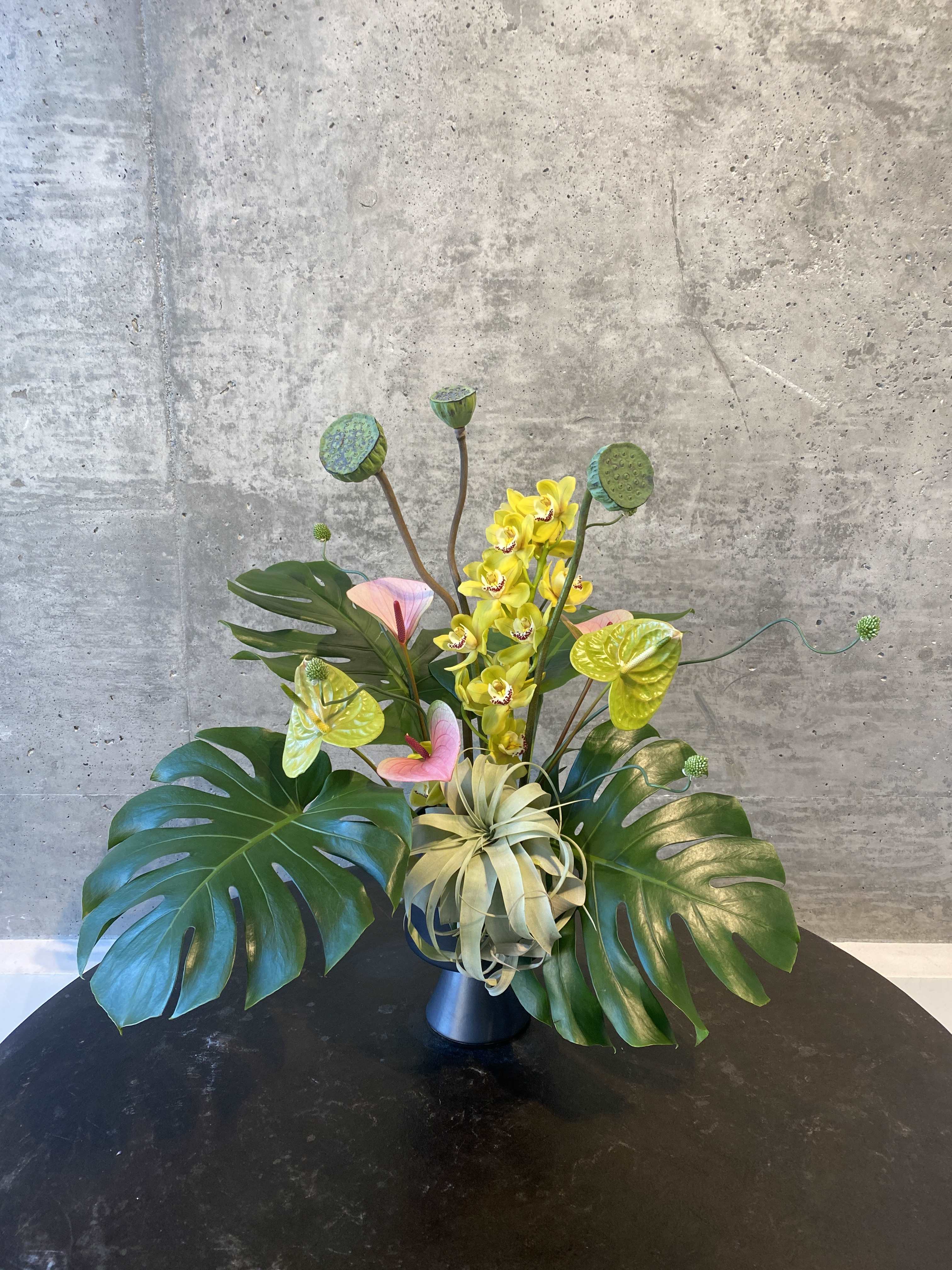 Tropical arrangement with yellow orchids and large monstera leaves in a vase