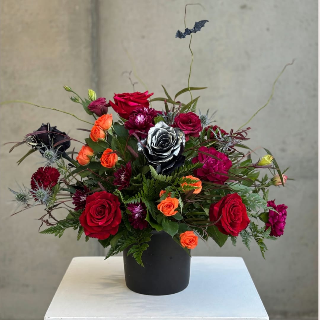 Mixed bouquet of red, orange, and purple roses in a black vase