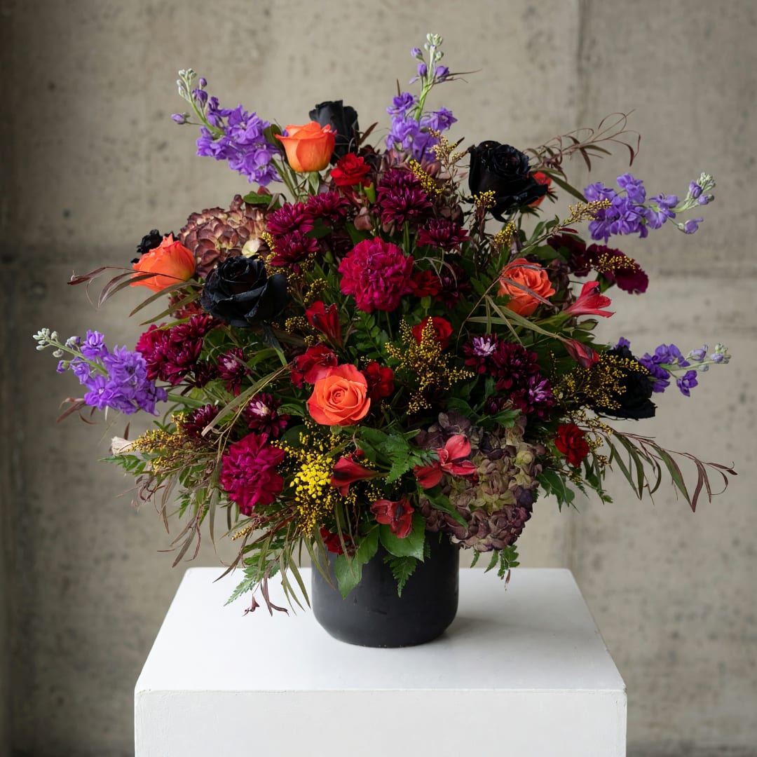Mixed bouquet in a black vase with orange, purple, red, and black flowers