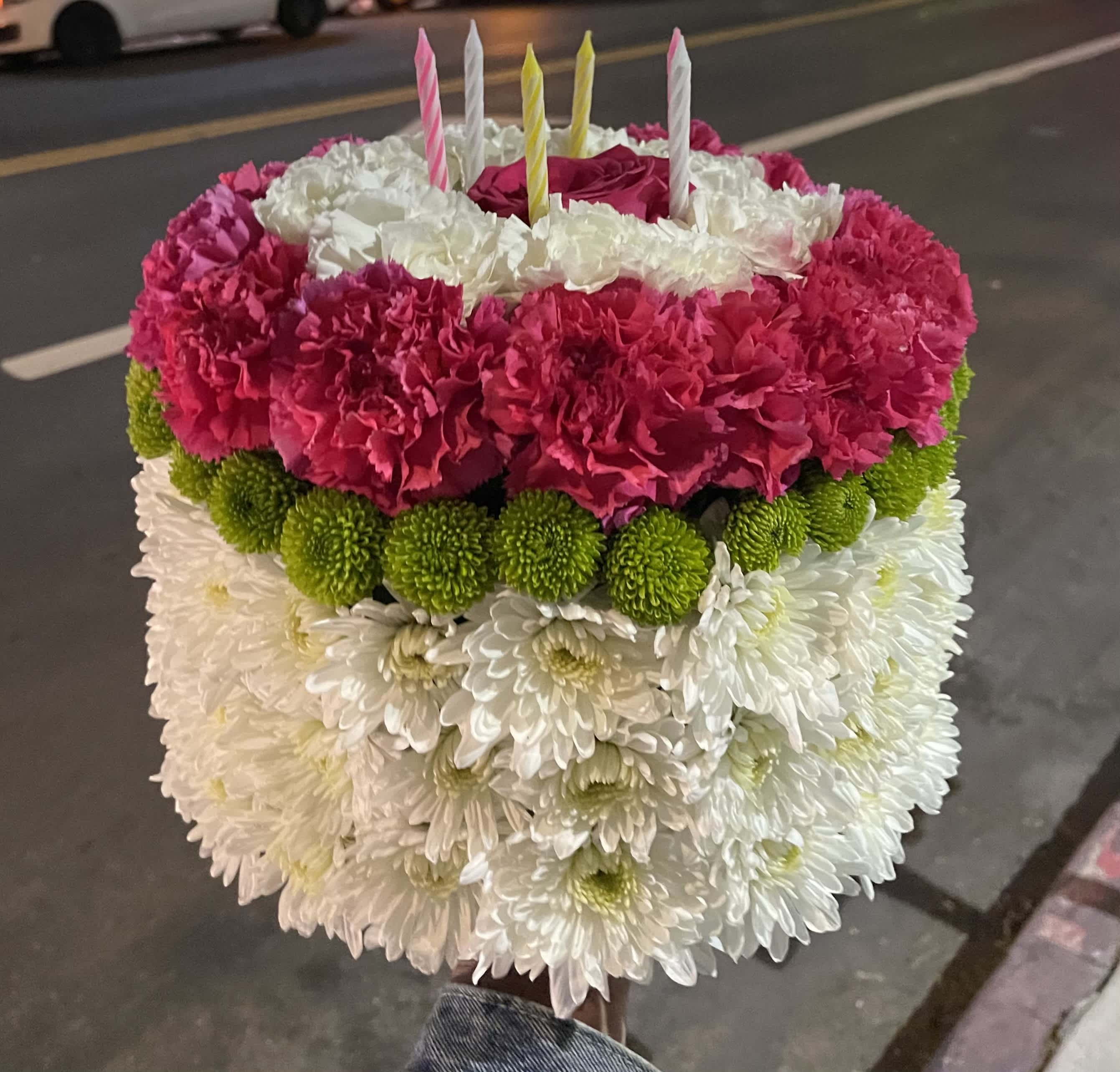Round floral cake with pink, white, and green flowers and striped candles