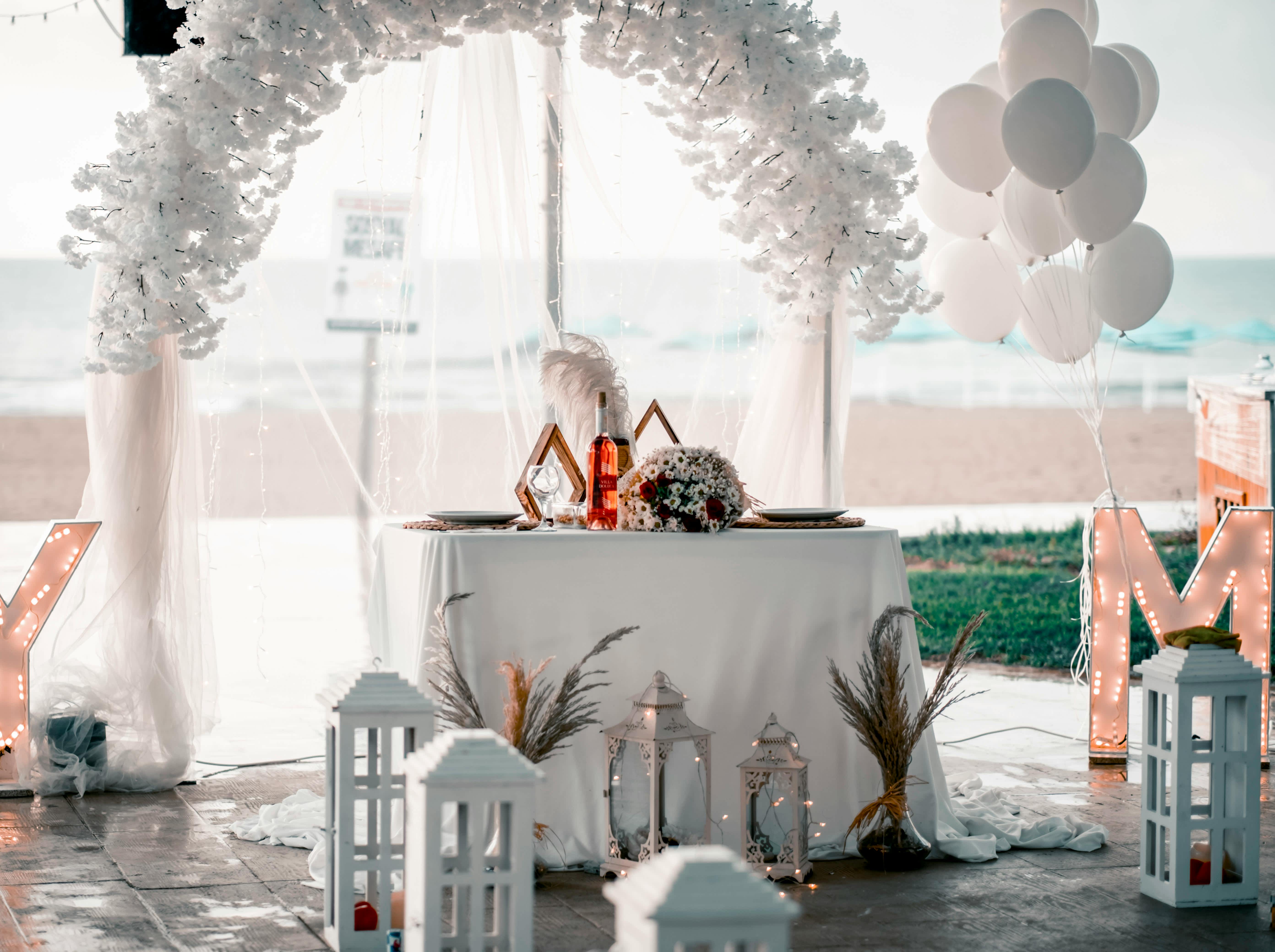 Beachside wedding table with white floral arch, balloons, and lanterns