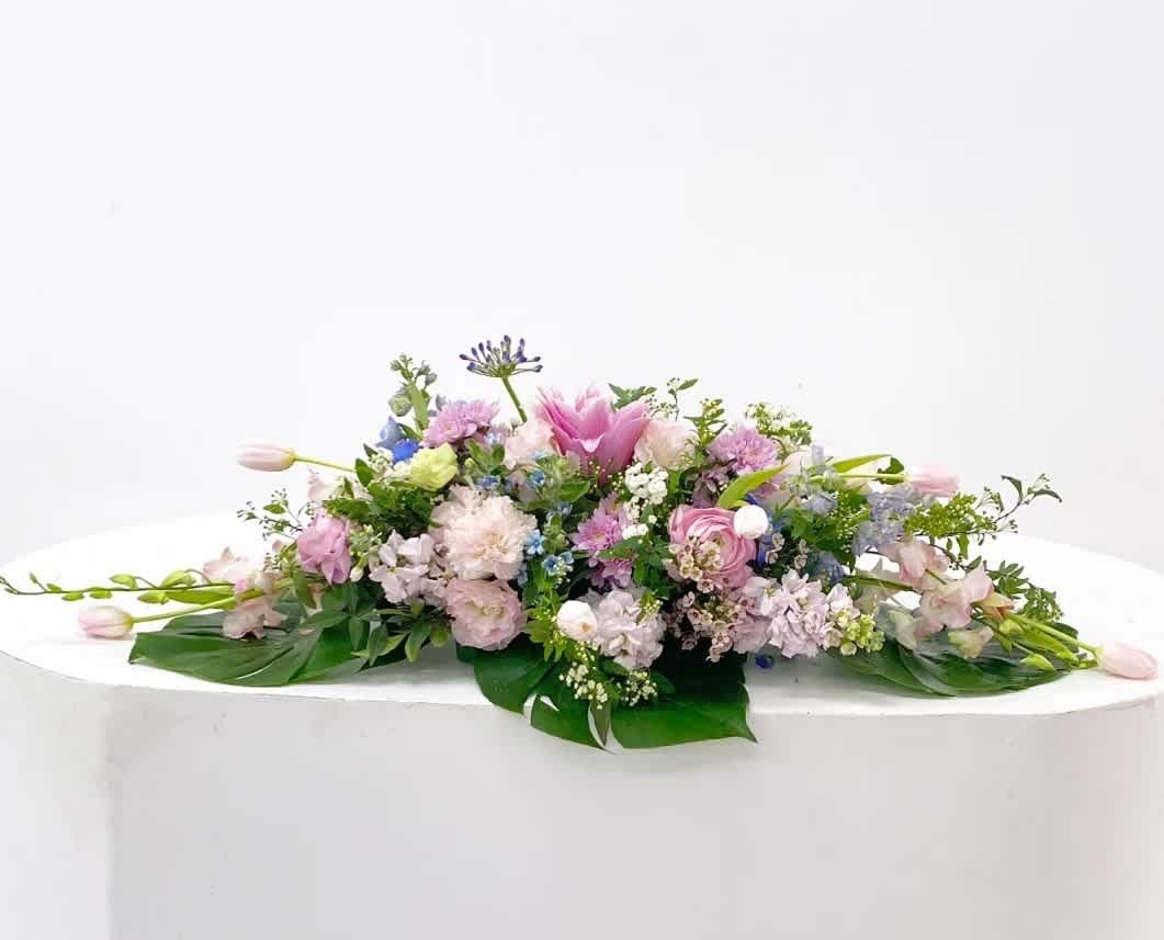 Low floral centerpiece with pink, lavender, and white blooms on a white table