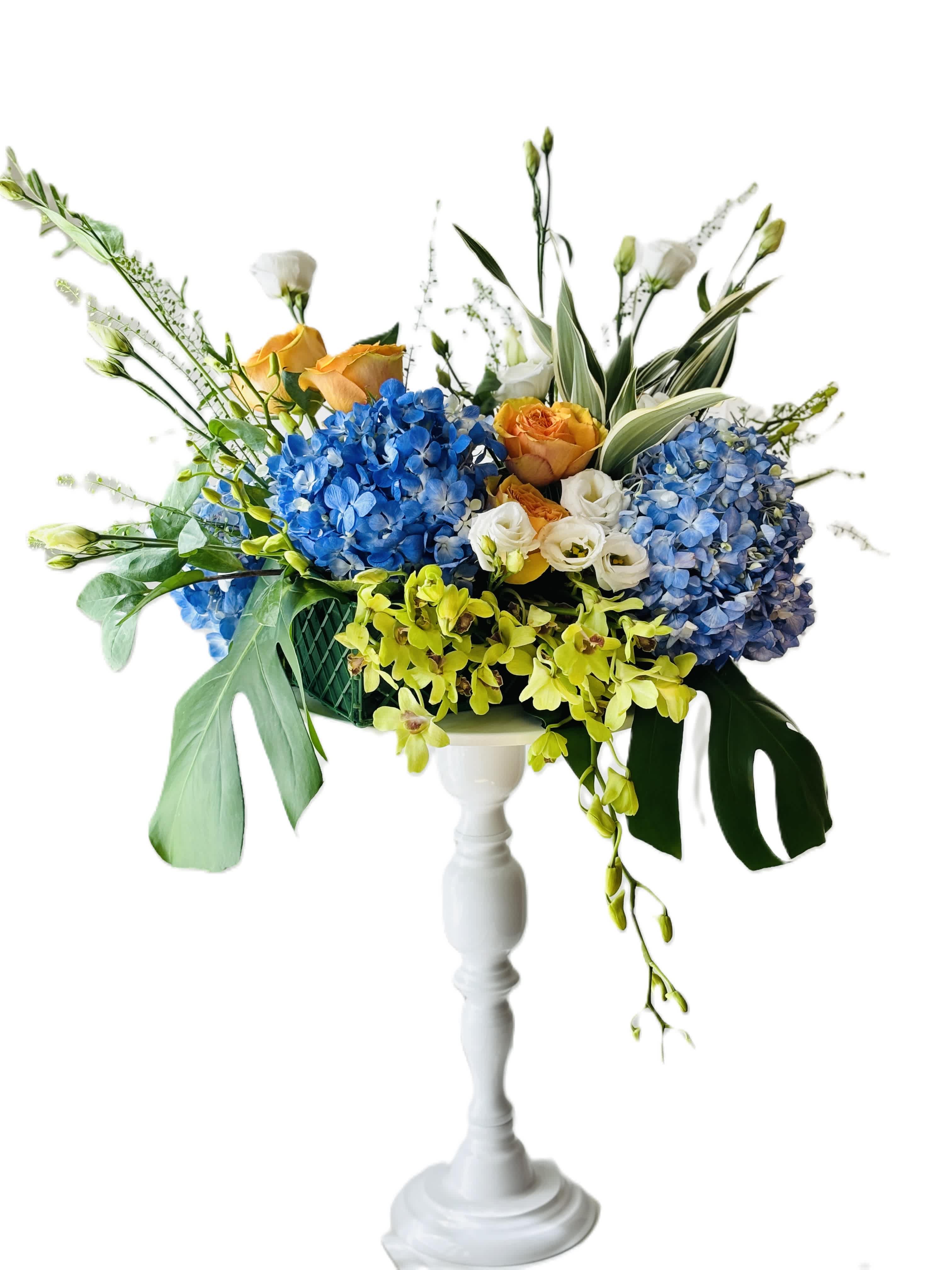 Blue hydrangea and orange rose arrangement in a white pedestal vase
