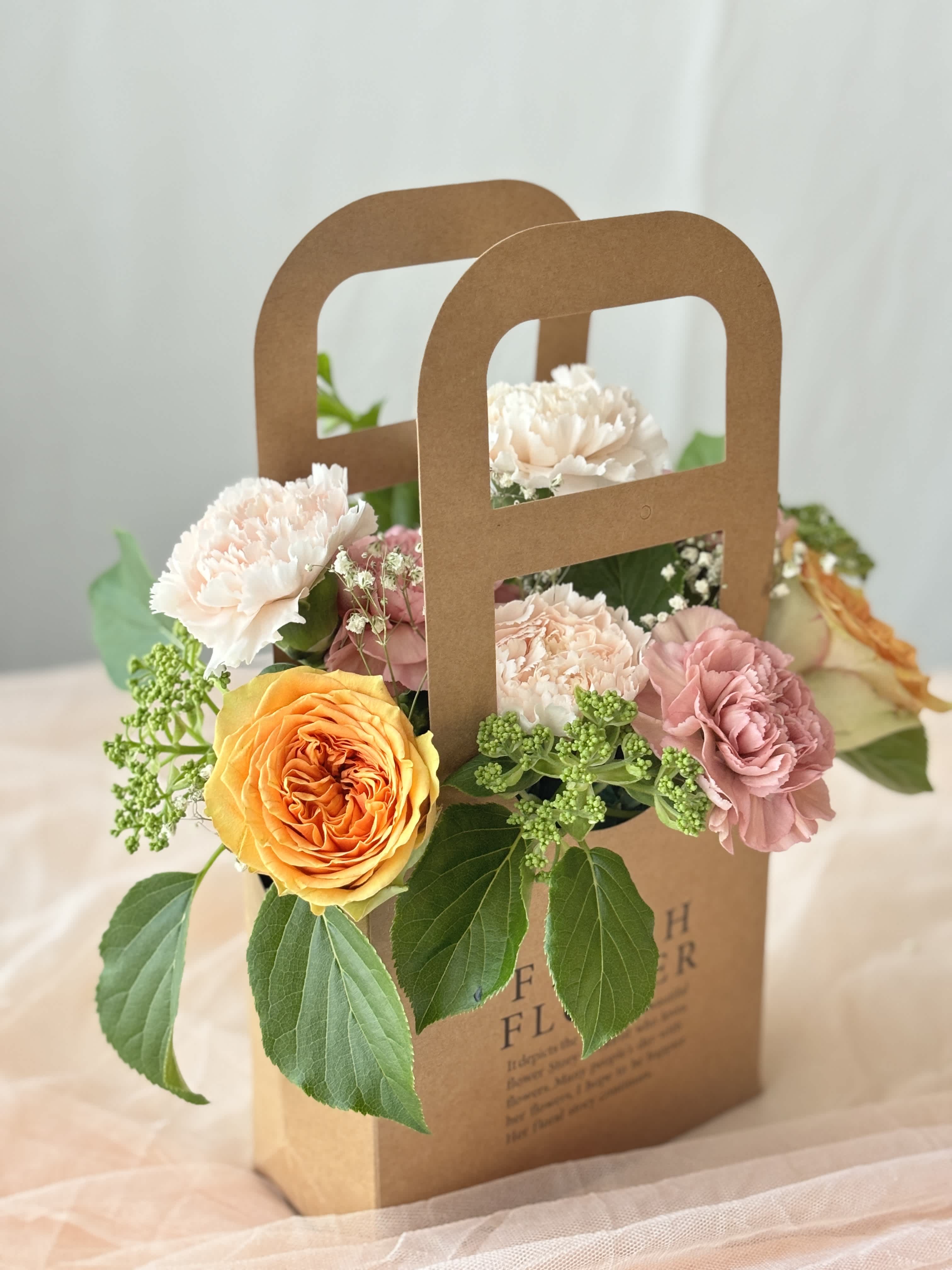 Mixed flowers arranged in a brown paper gift bag with handle cutouts