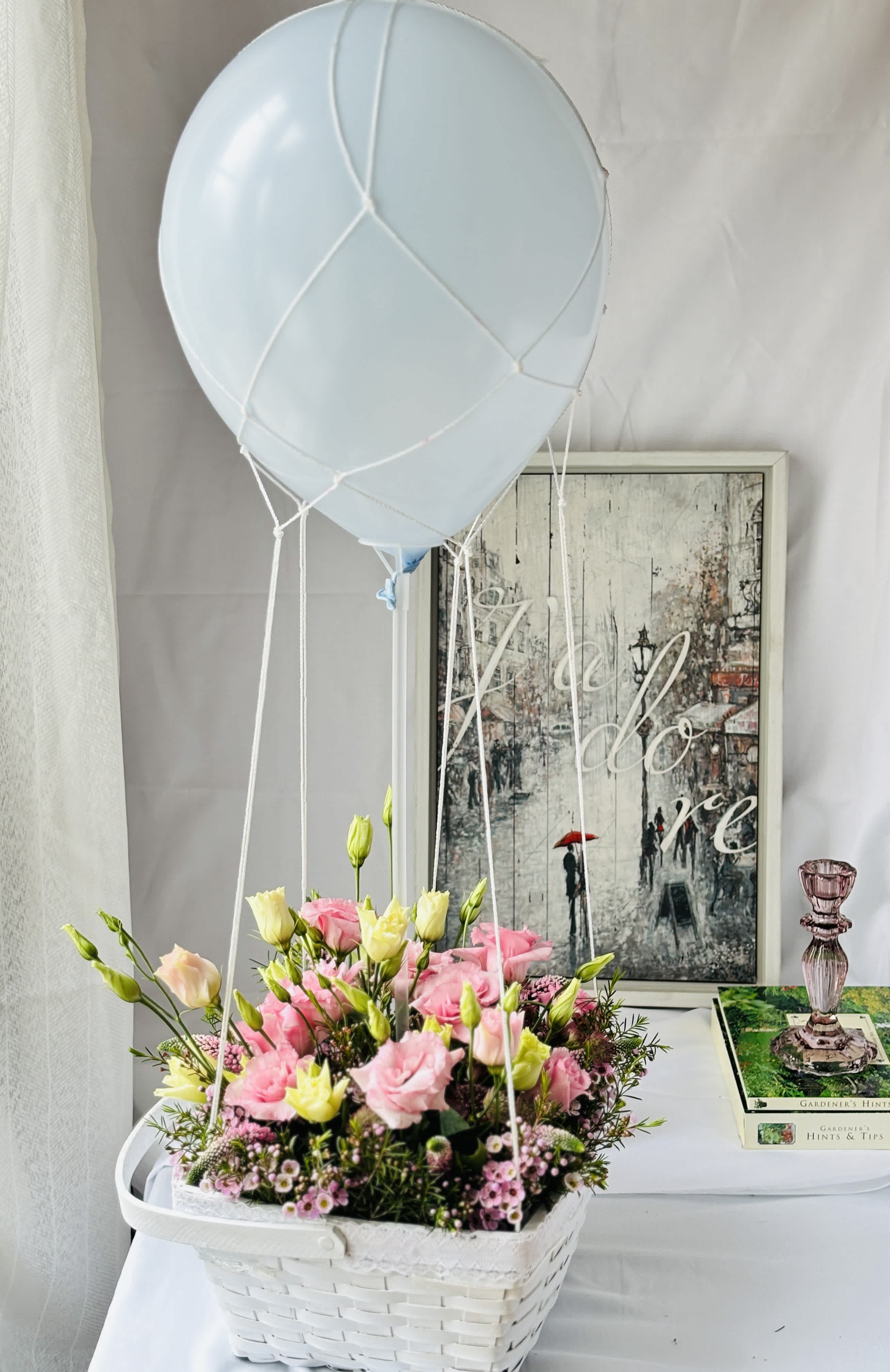 Pink and cream flowers in a white basket with a pale blue balloon