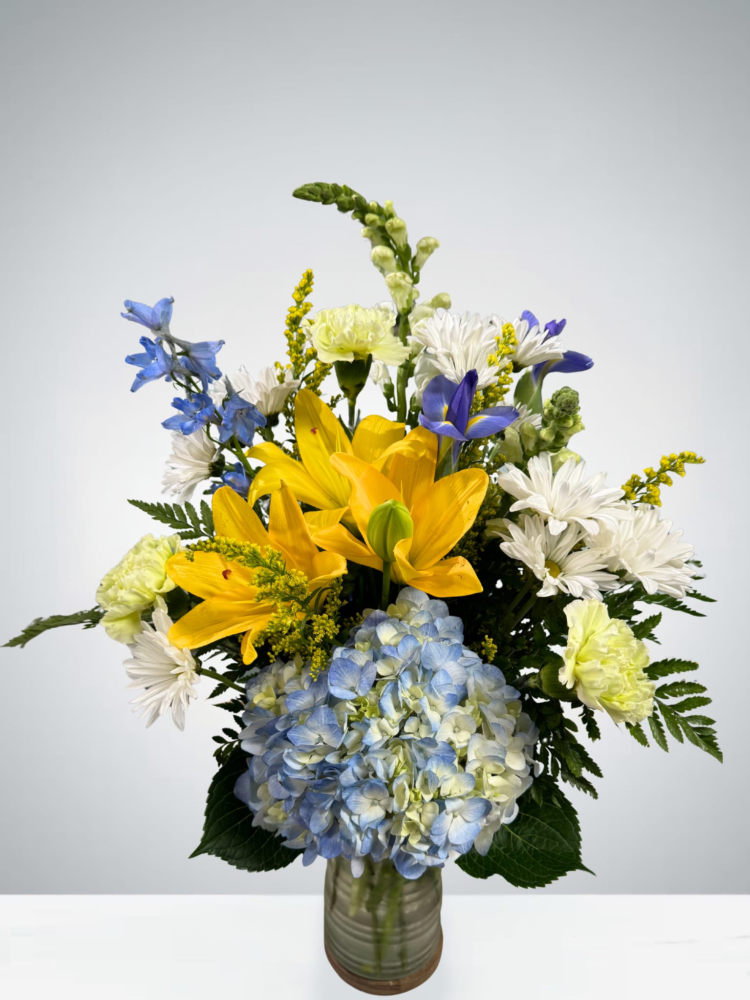 Bouquet of yellow lilies, blue hydrangea, and white daisies in a glass vase