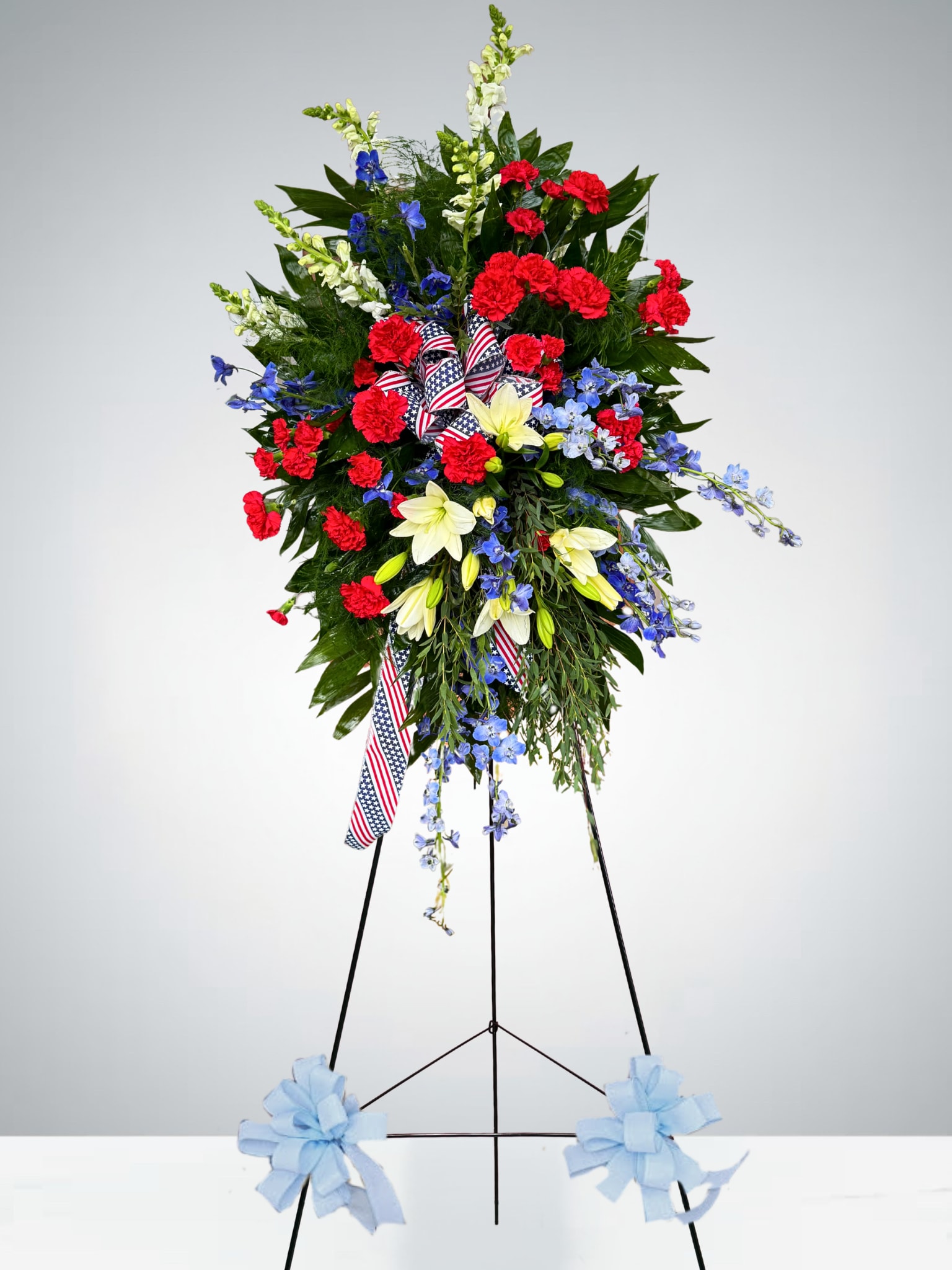 Standing floral spray with red, white, and blue flowers on a tripod easel