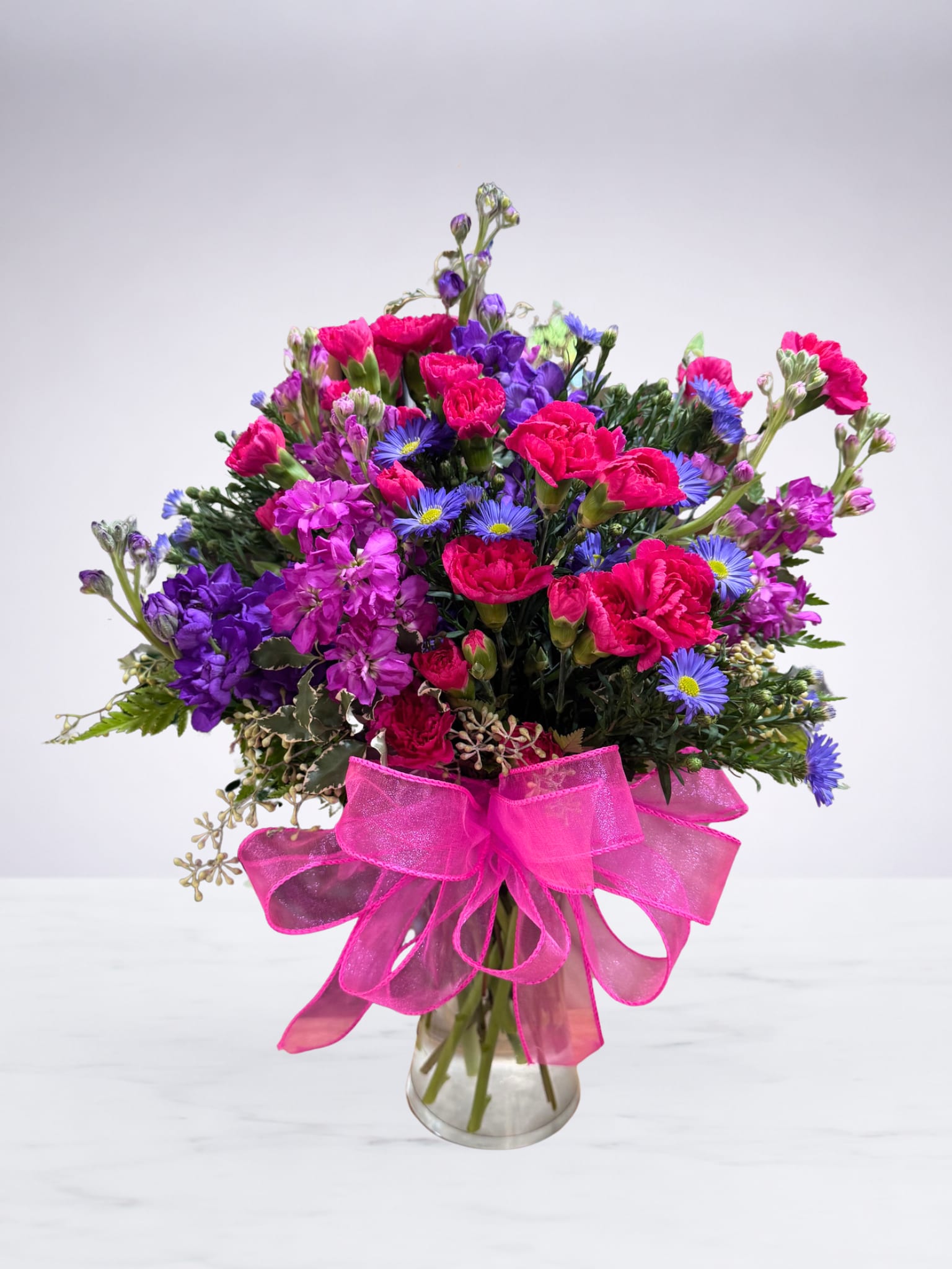 Colorful bouquet of pink, purple, and blue flowers in a glass vase with a pink ribbon
