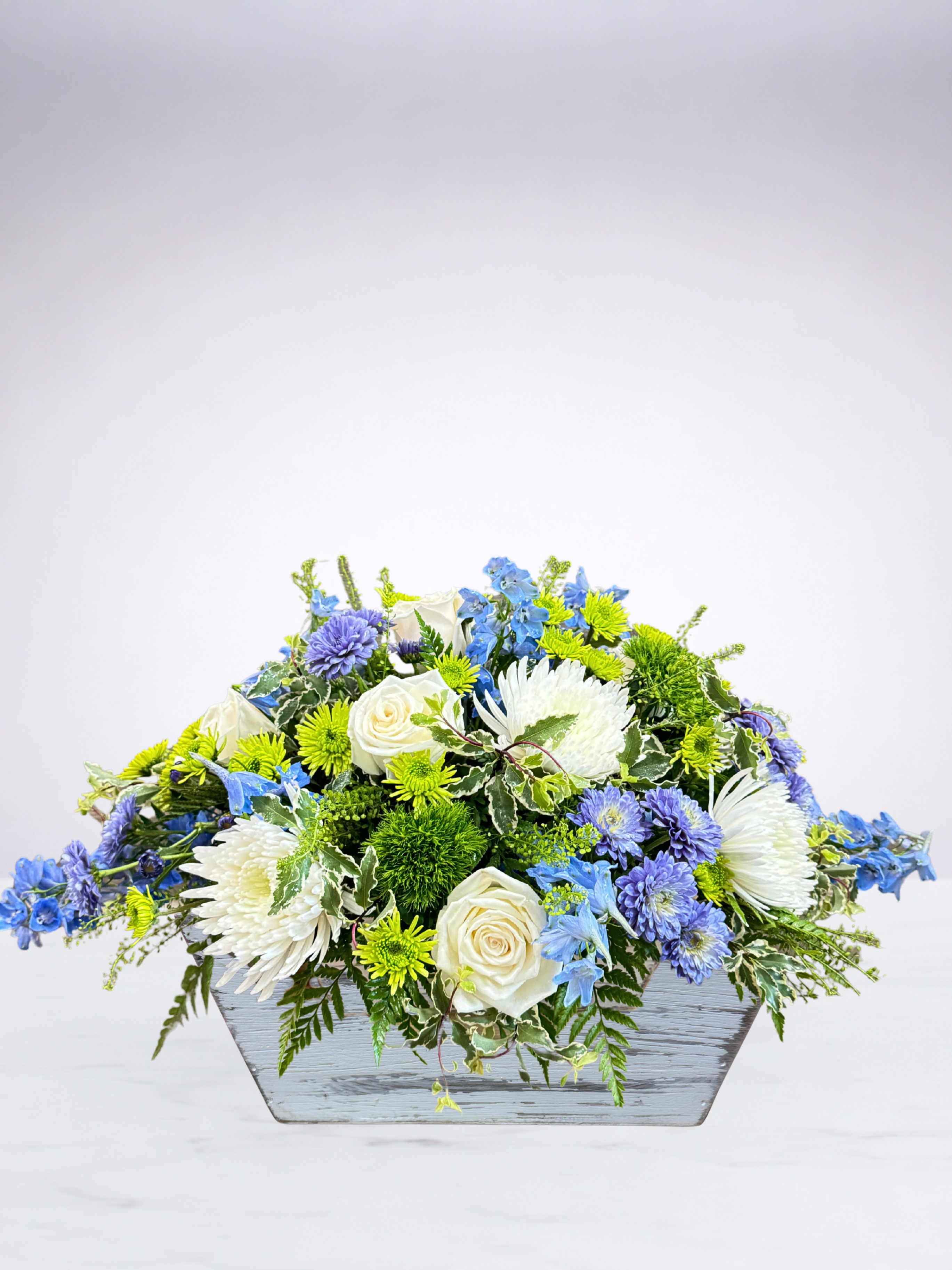 Blue, white, and green floral arrangement in a gray wooden container