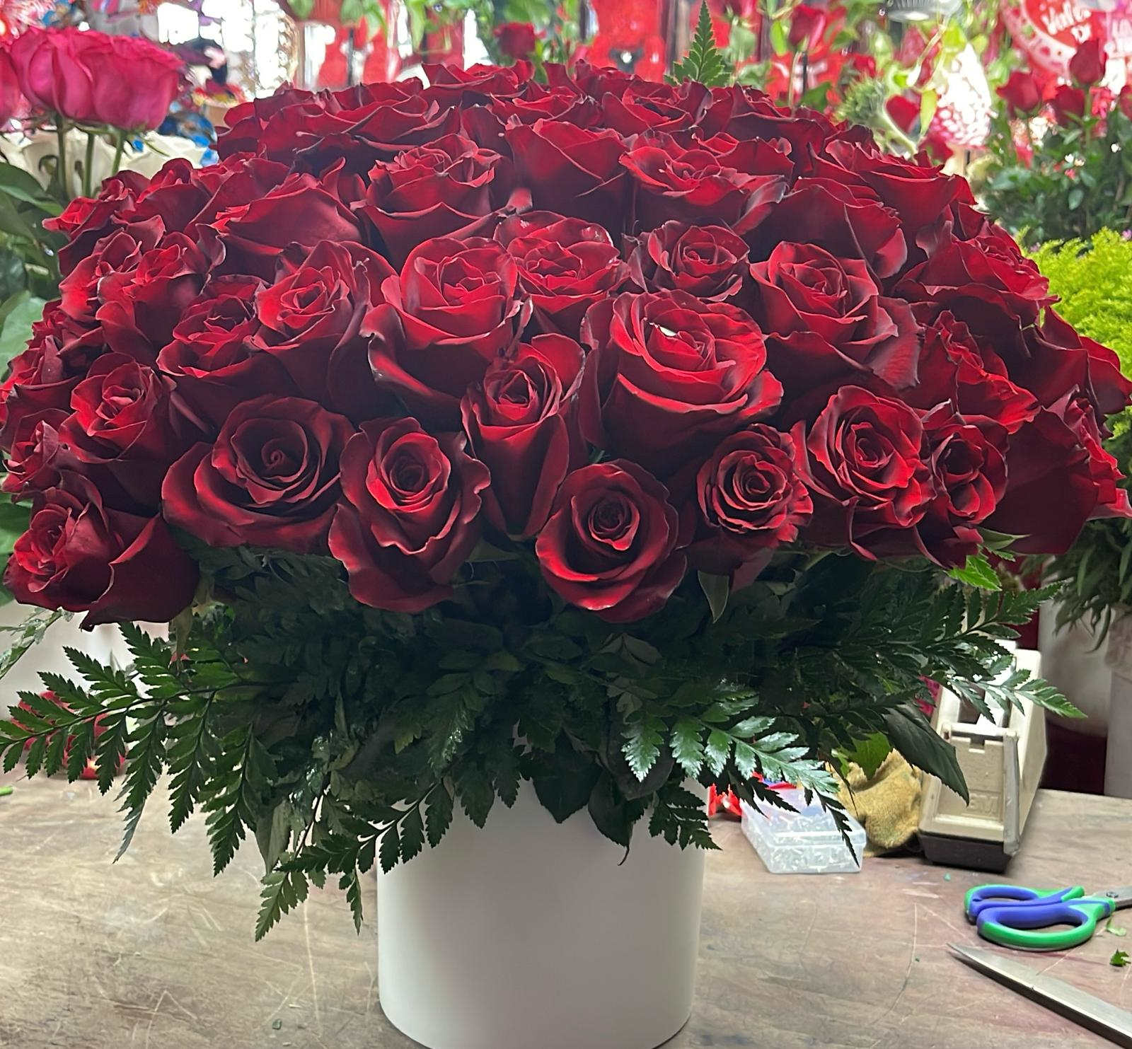 Large bouquet of red roses in a white vase with fern foliage