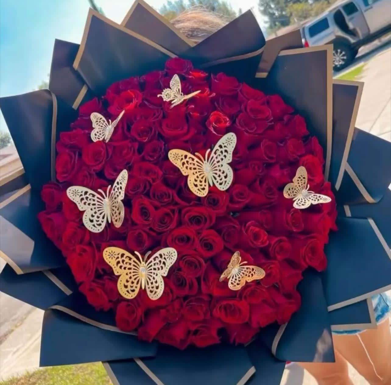 Round bouquet of red roses with decorative butterfly accents.