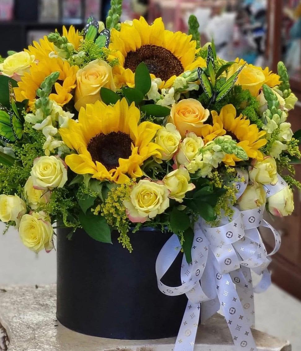 Yellow sunflowers and roses arranged in a black box with a white ribbon.
