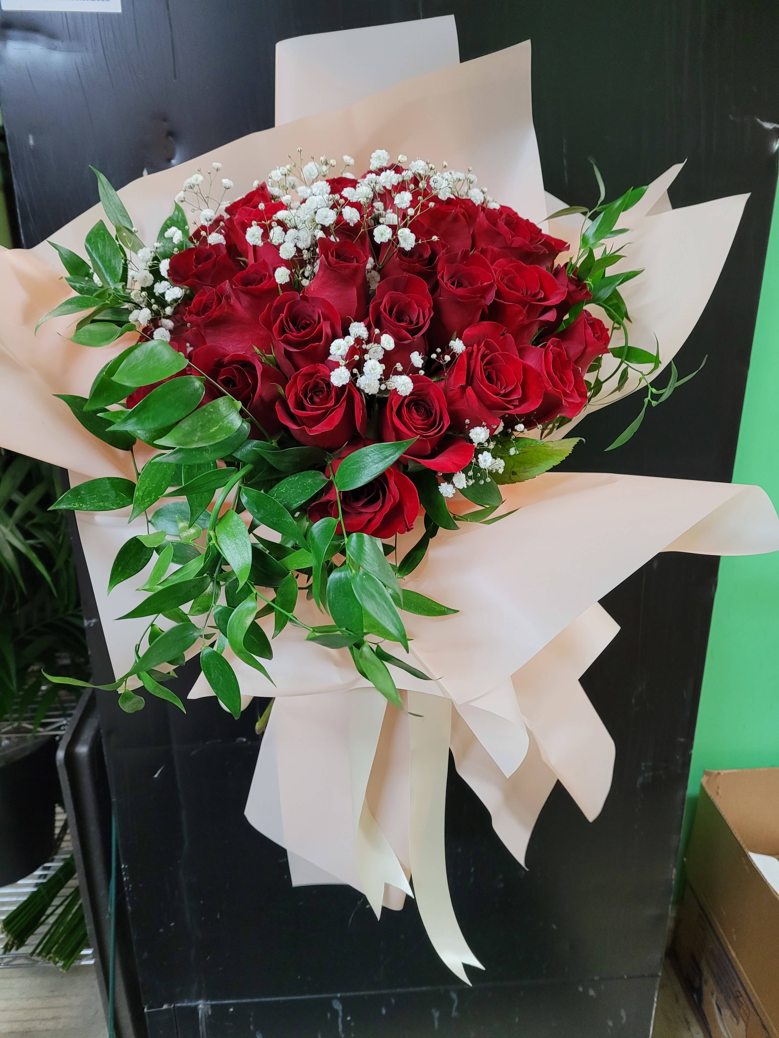 Bouquet of red roses with white baby's breath and greenery in cream wrap