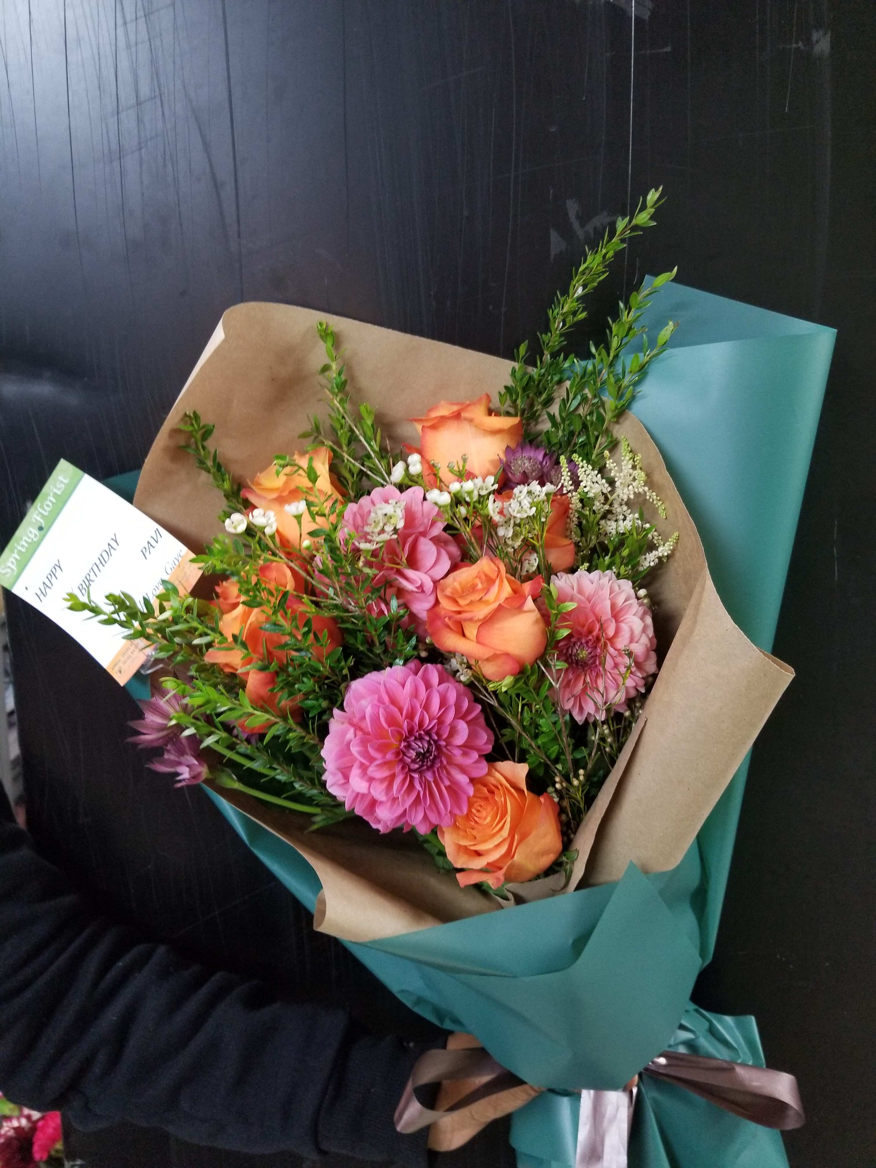 Bouquet of orange roses and pink dahlias wrapped in brown and teal paper
