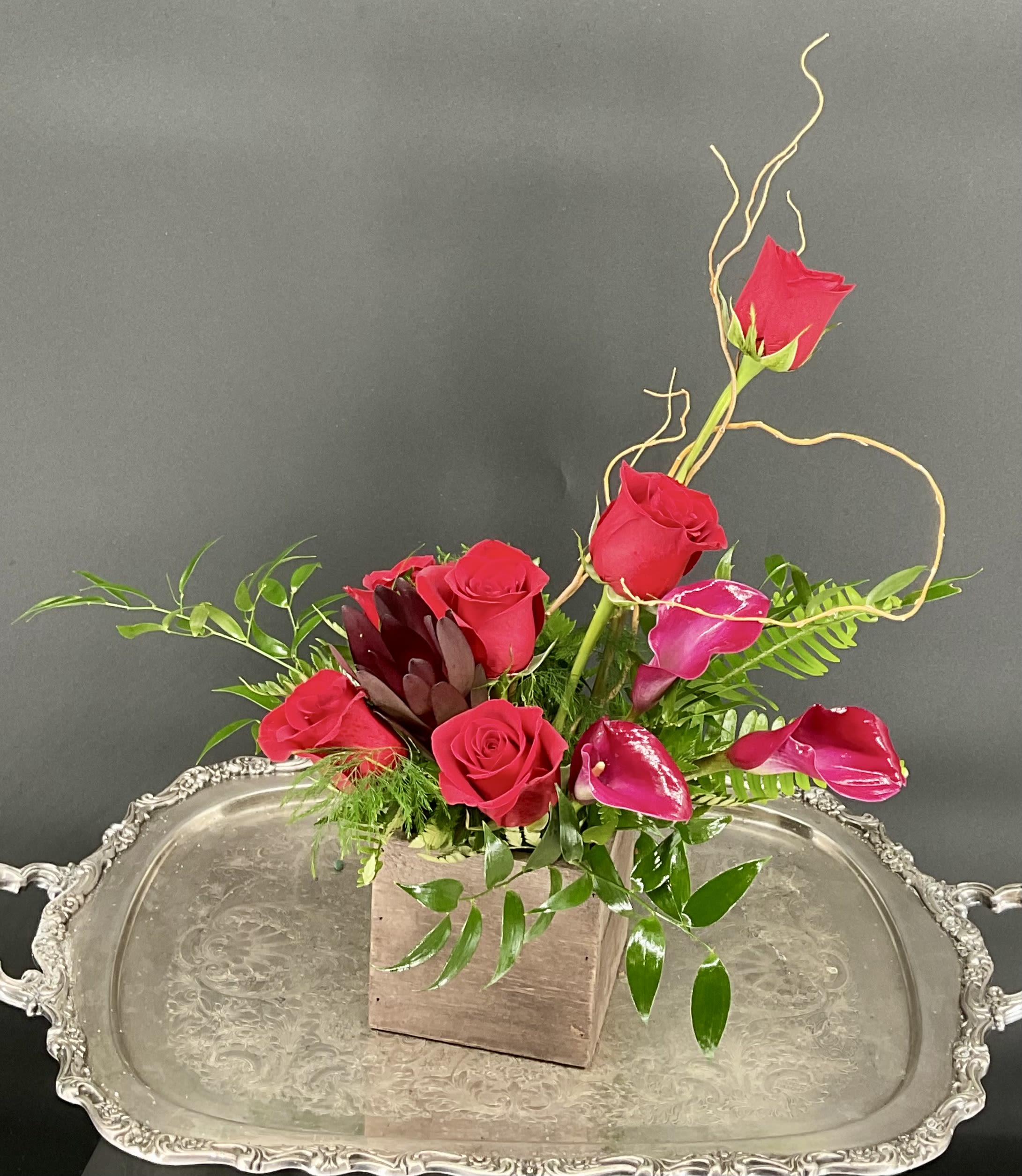 Red roses and pink calla lilies arranged in a square wooden vase
