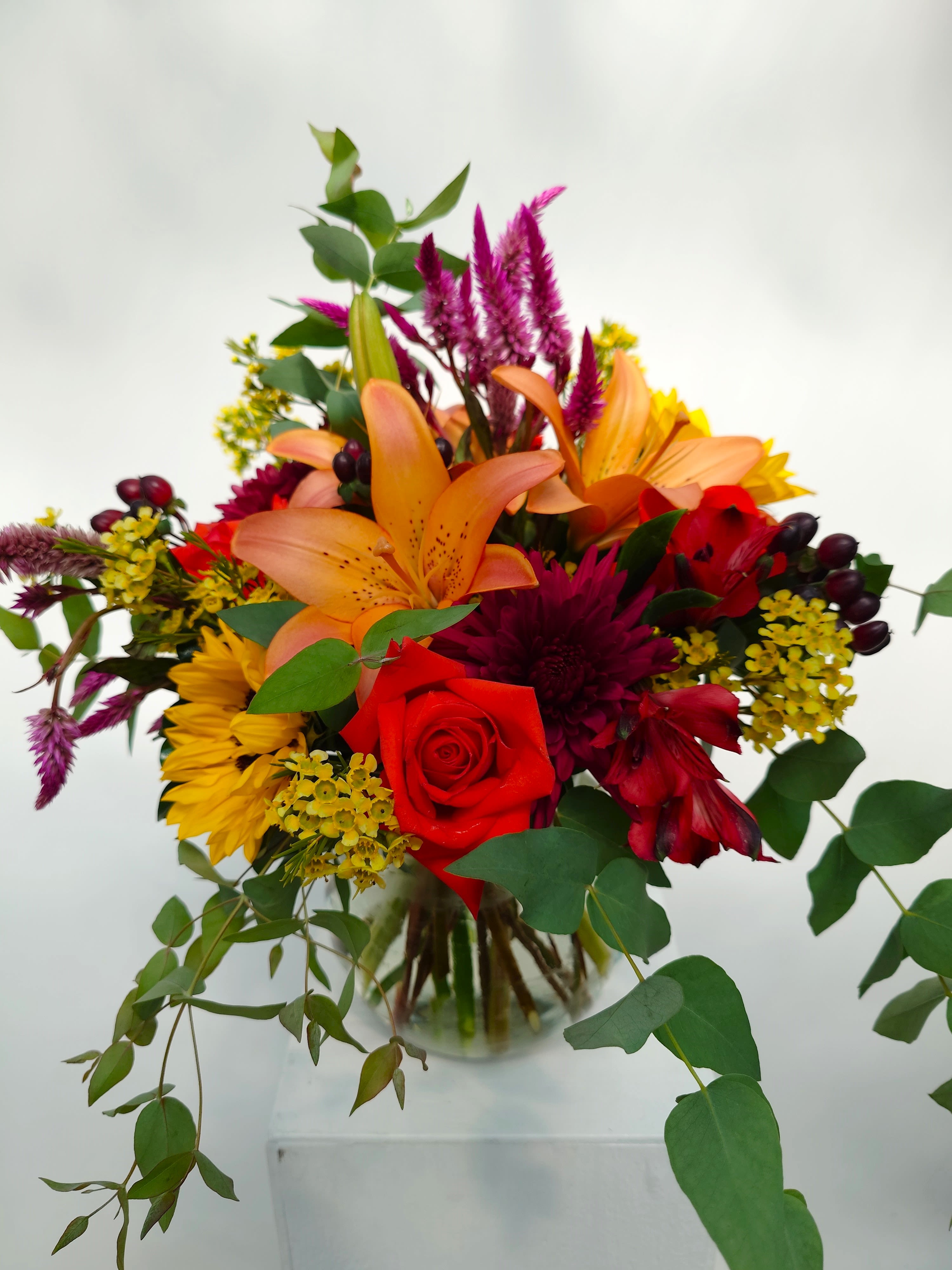Mixed bouquet with orange lilies, red roses, and yellow flowers in a glass vase