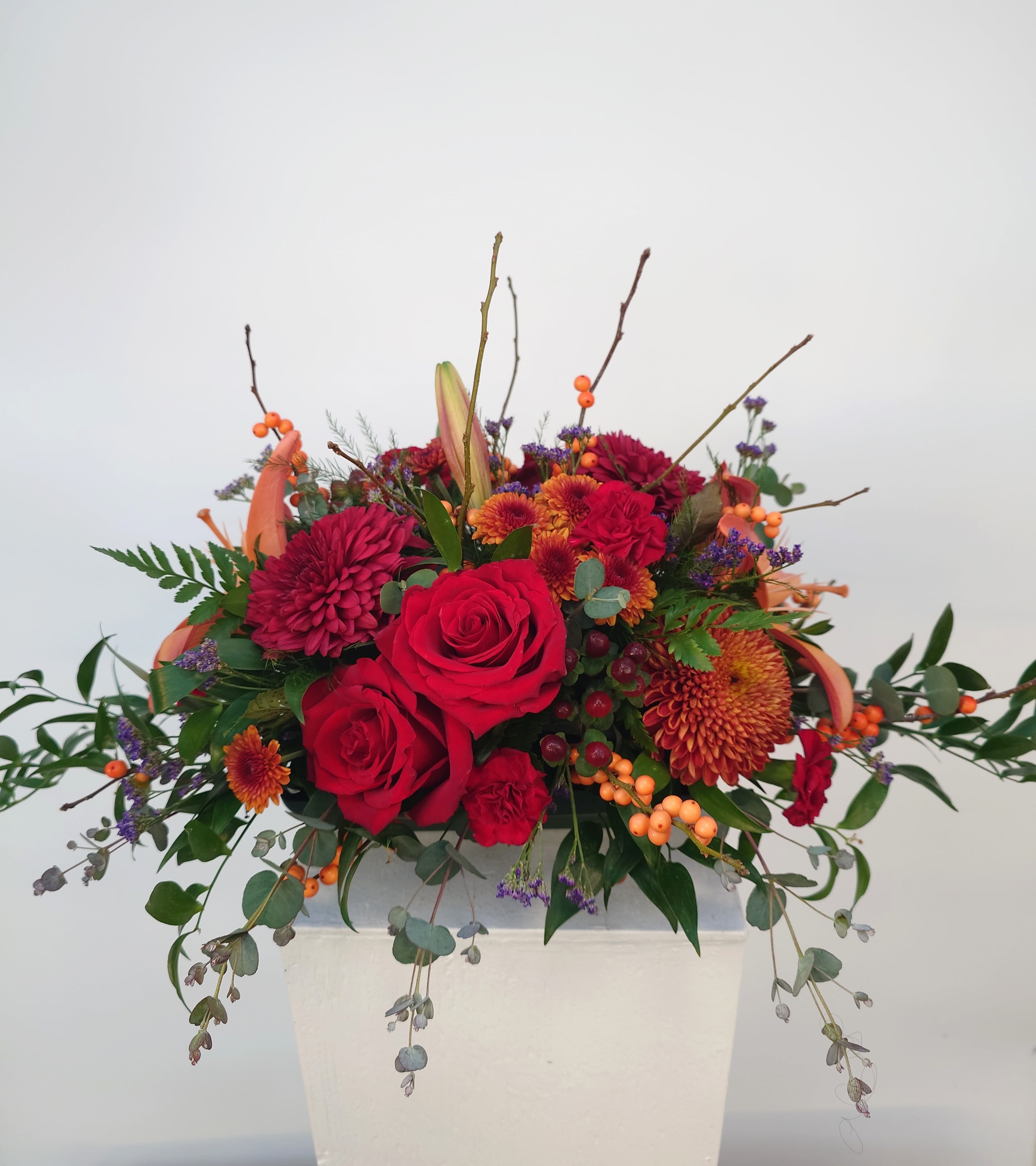Red roses and orange mums in a white vase with trailing greenery
